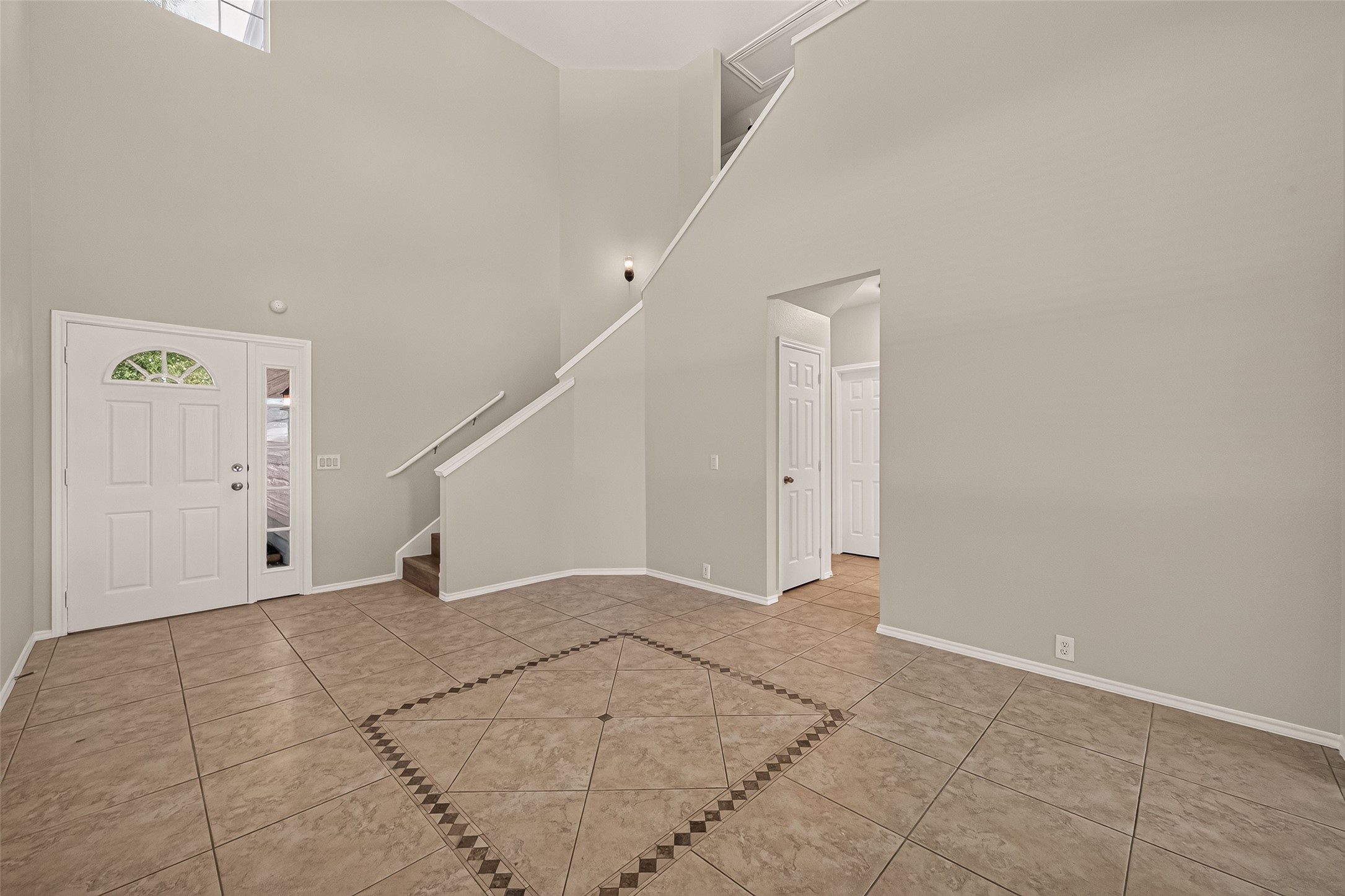 This photo showcases a spacious, light-filled entryway with high ceilings and elegant tile flooring. It features a staircase leading to the upper level and a doorway to an adjacent room, offering a welcoming and open feel.