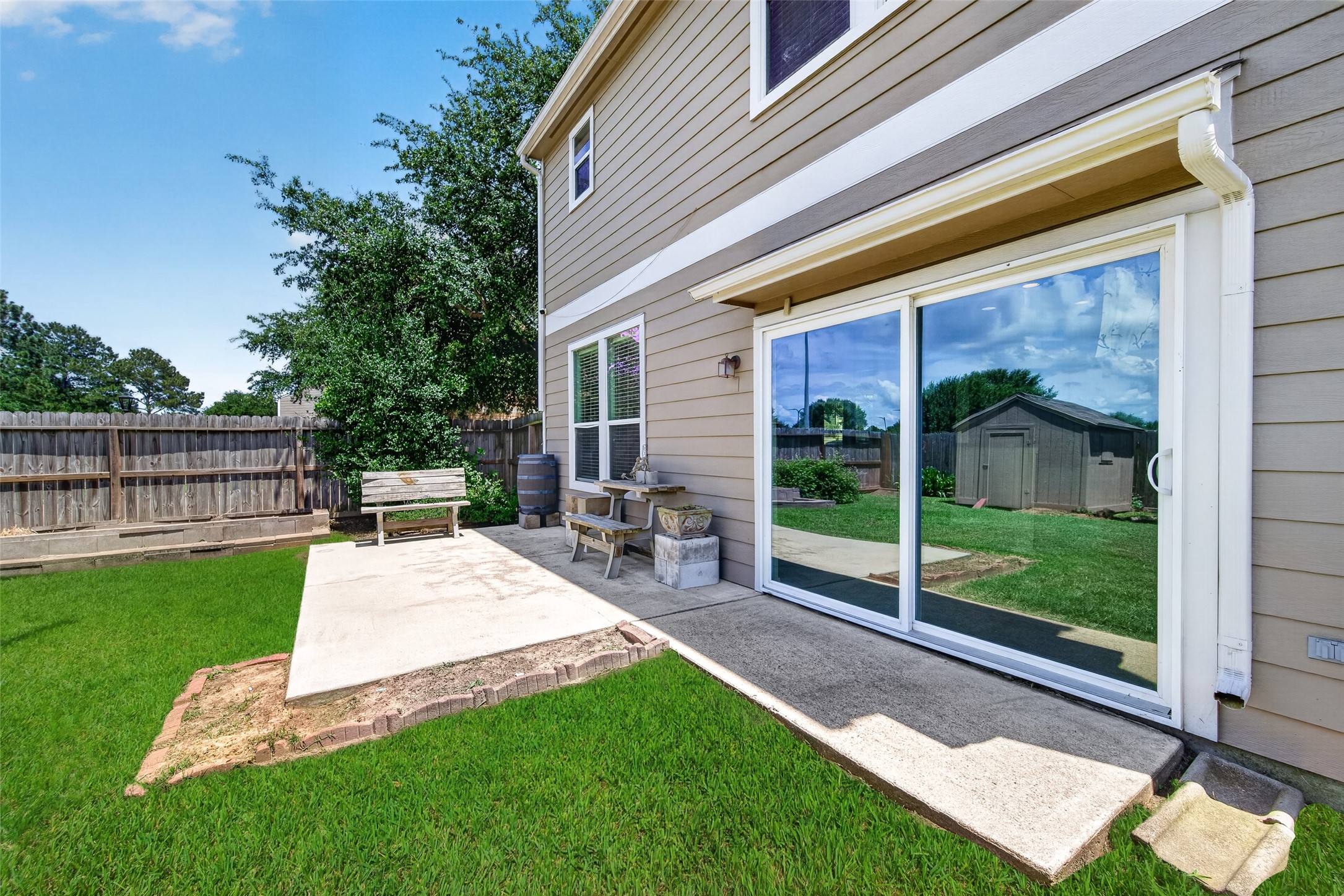 Spacious backyard with lush green lawn, a small shed, and a concrete patio area perfect for outdoor seating. Ideal for relaxation and gardening.