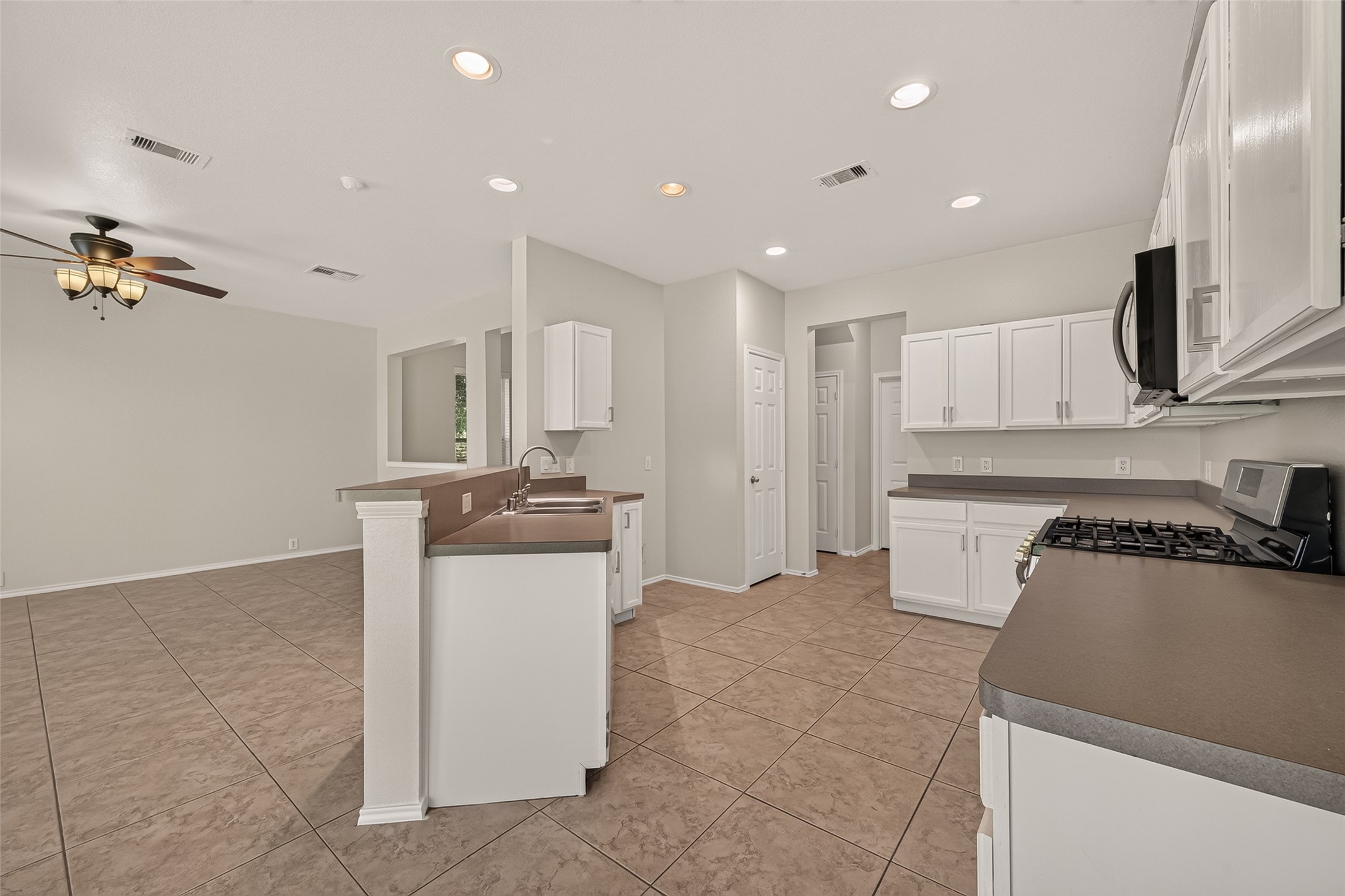 This photo showcases a spacious kitchen with modern appliances, white cabinetry, and a brown countertop. The open layout extends into a living area with tiled flooring and a ceiling fan, creating an inviting space perfect for entertaining.