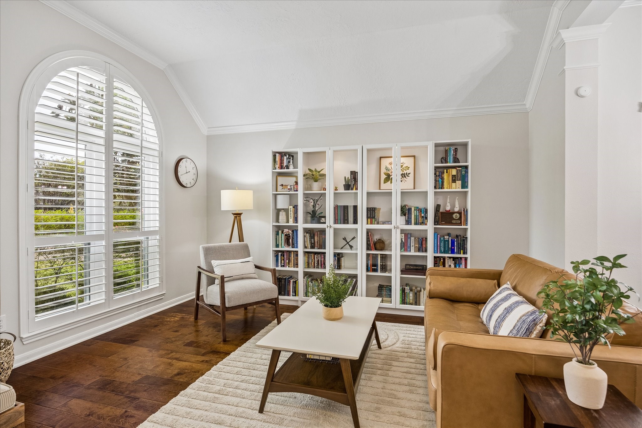 Timeless elegance meets everyday comfort! Gorgeous arched windows with plantation shutters fill this beautifully appointed living room with natural light, while rich wood flooring and graceful architectural details create a warm, sophisticated atmosphere.