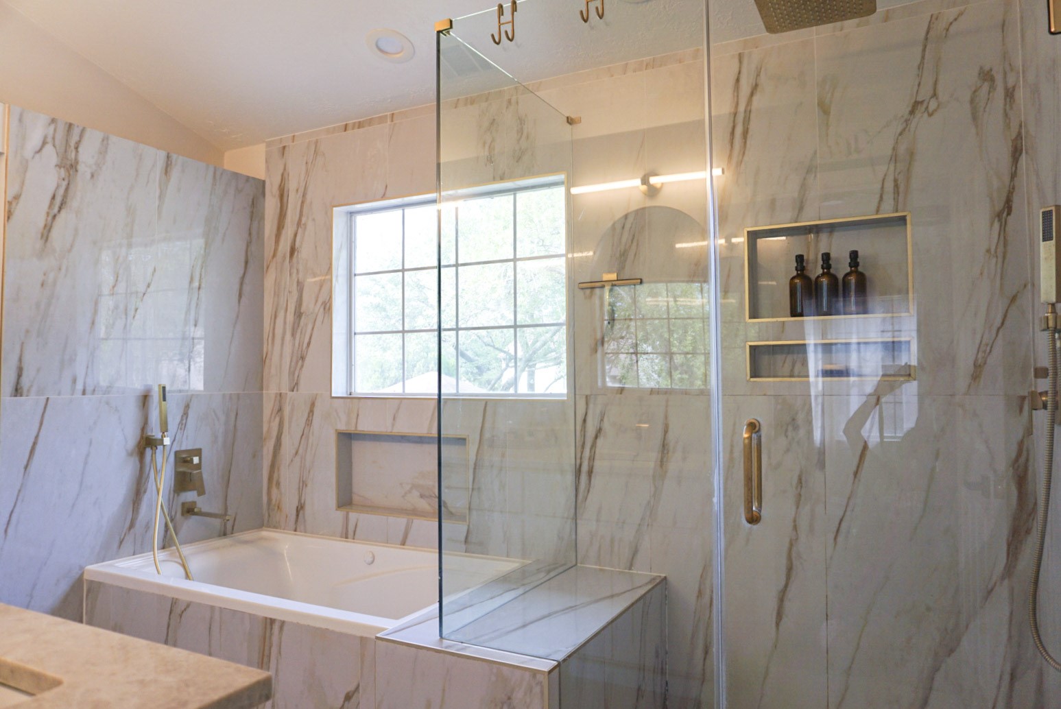 Walk-in rainfall shower with bench and hand-held attachment, jetted tub with Roman faucet, full tiled wall