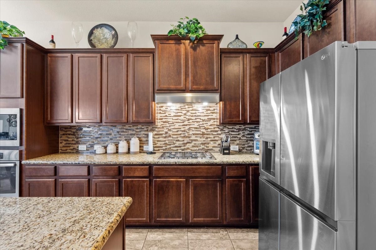 Rich wood cabinetry, tile backsplash, and stainless steel refrigerator.