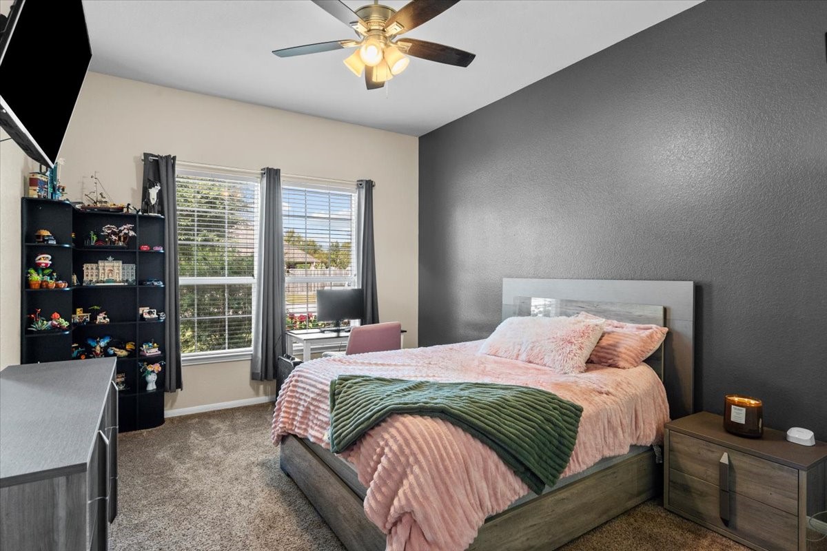 Secondary bedroom with accent wall, ceiling fan, and a bright window.