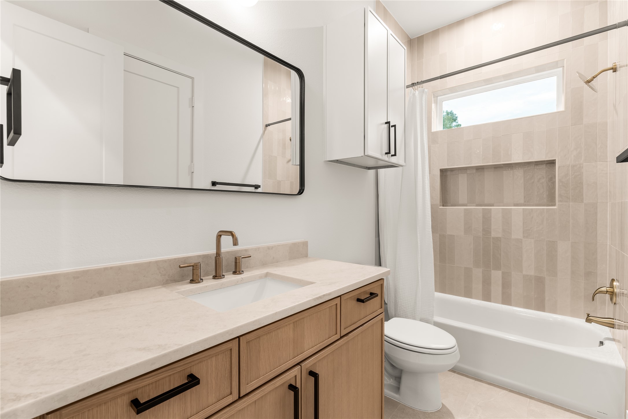 Stylish full secondary bathroom featuring warm wood cabinetry, quartz countertops, matte black hardware, and custom tilework.