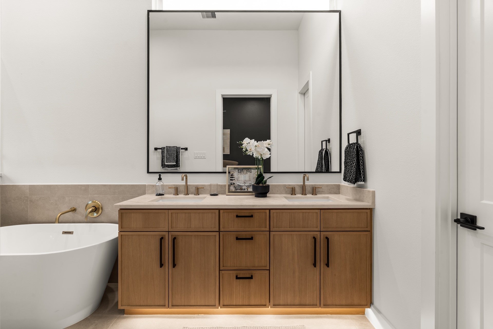 Spa-inspired primary vanity featuring dual undermount sinks, ambient toe-kick lighting, and custom warm wood cabinetry.