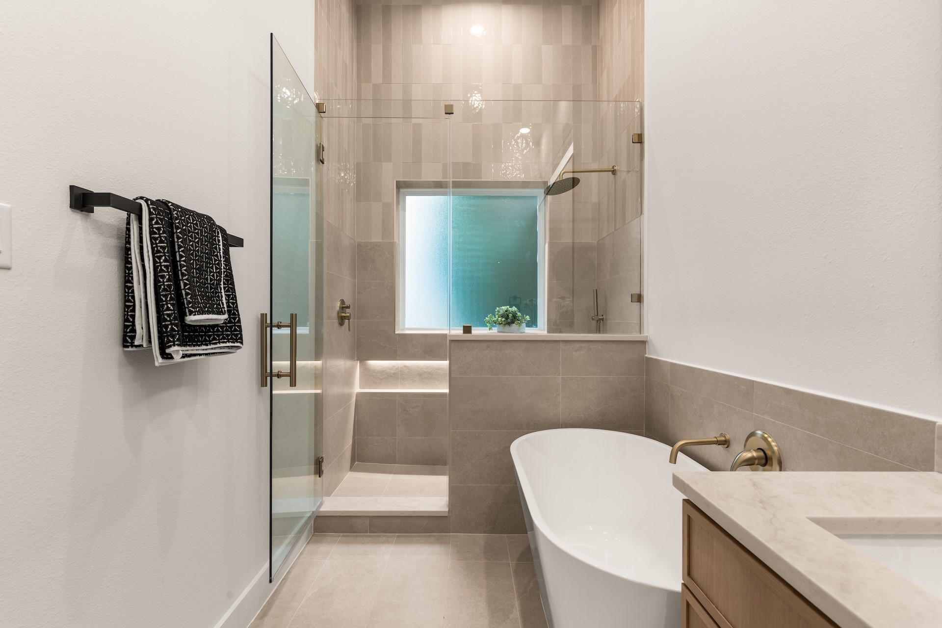 Modern primary shower space featuring floor-to-ceiling tilework, niche storage, and warm brass fixtures.