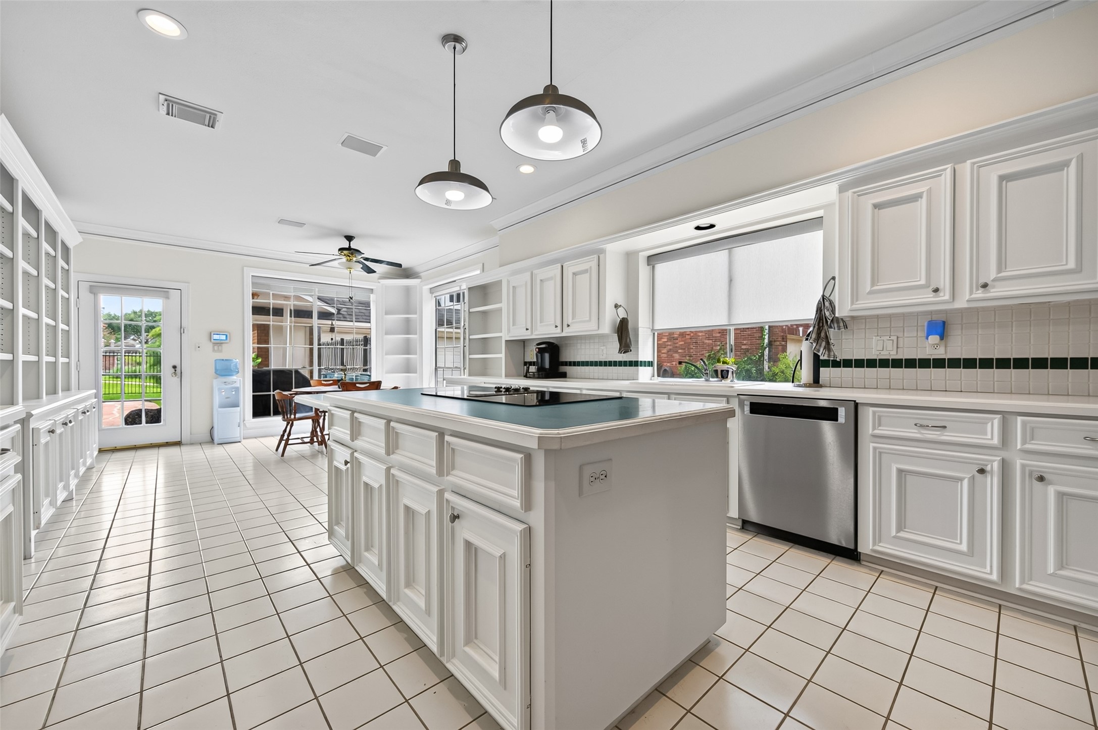 Spacious kitchen with white cabinetry, a large island, and modern appliances, featuring ample natural light from large windows and a door leading to the outdoor area.