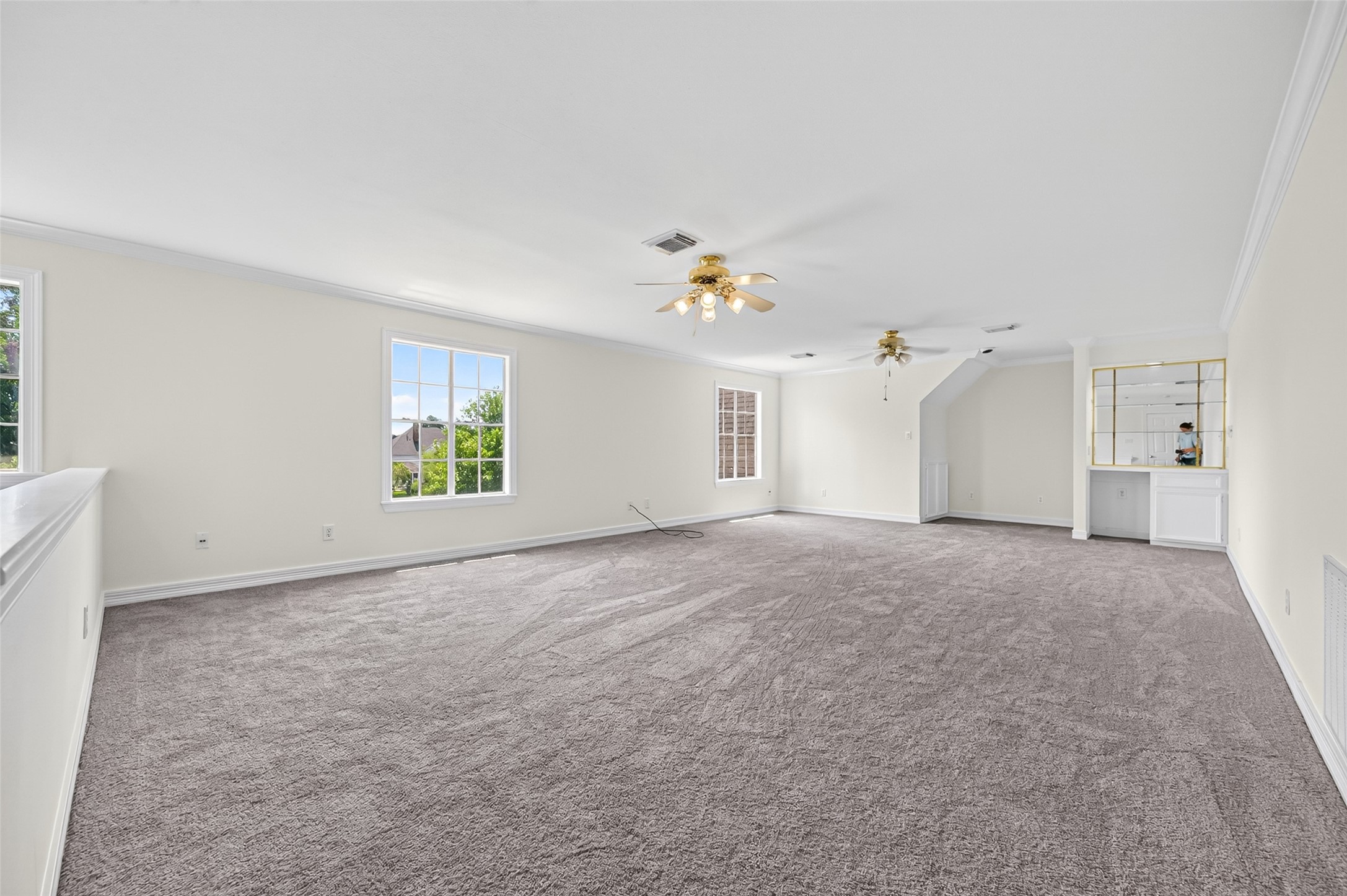 Spacious and bright carpeted room with large windows, ceiling fans, perfect for entertaining or relaxation.