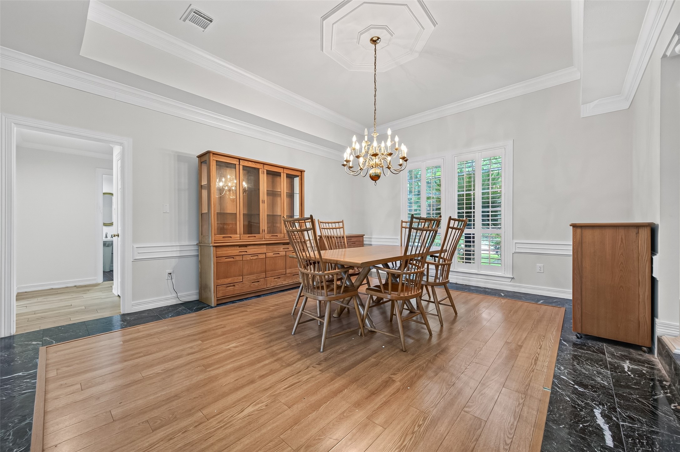 Elegant dining room featuring a classic chandelier, and abundant natural light through large windows with shutters.