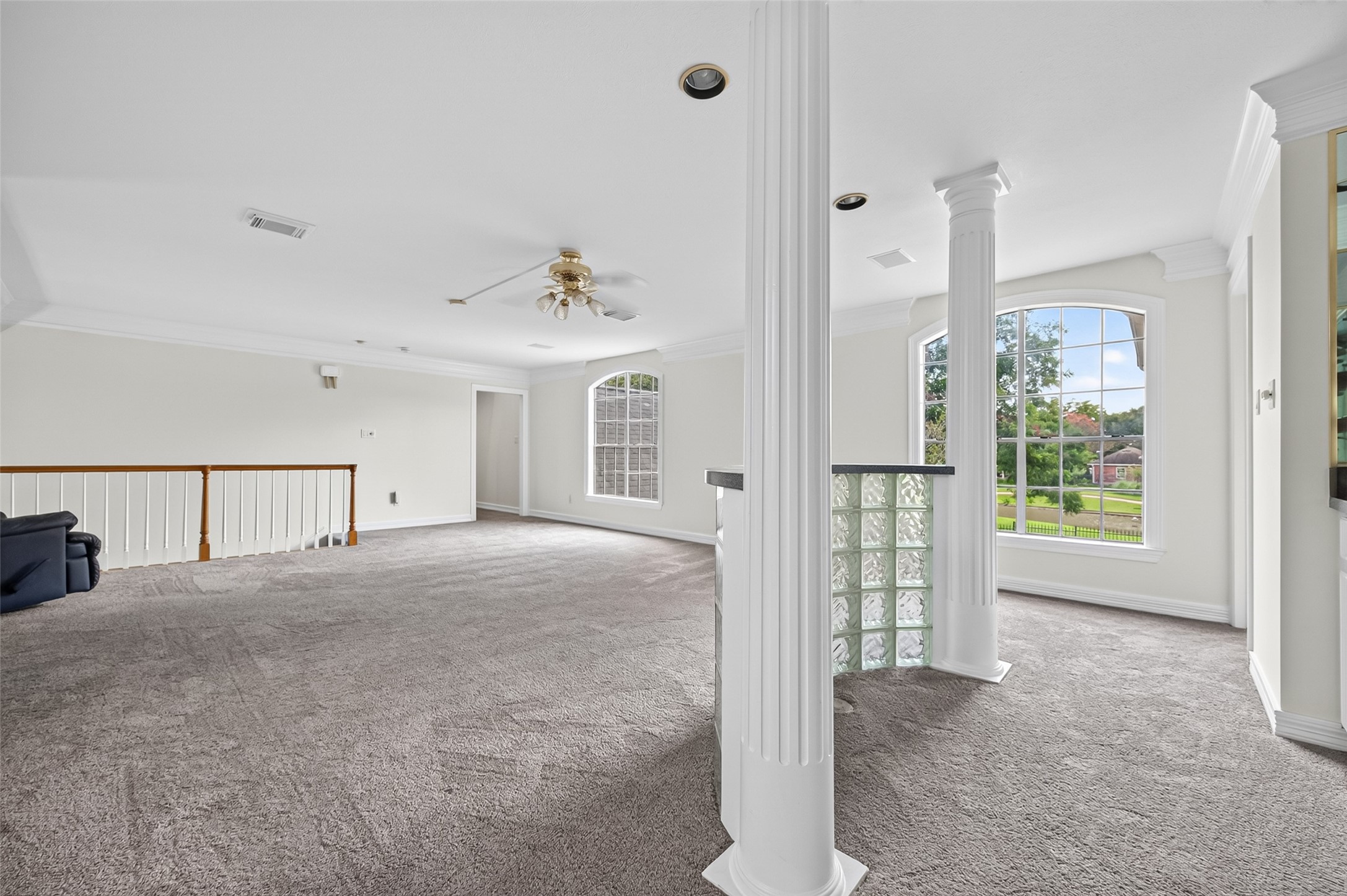 Another view of the spacious and bright living area featuring large windows, elegant columns, and carpeting, perfect for relaxation and entertainment.