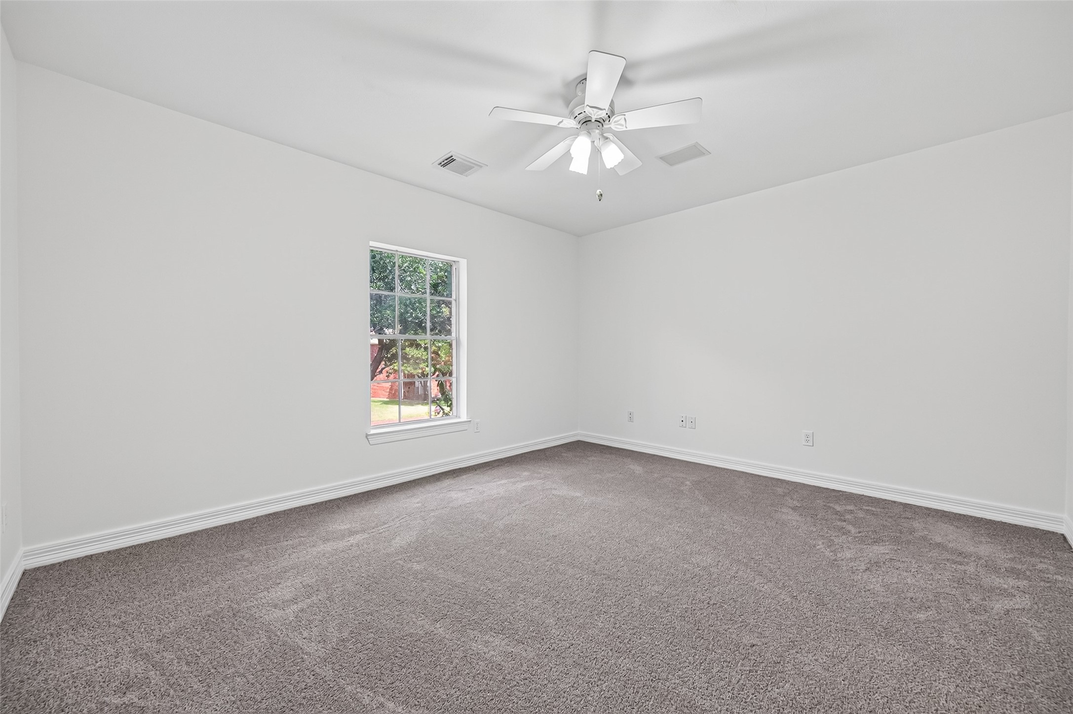 Bright and spacious bedroom featuring recent carpeting, a ceiling fan, and a large window inviting natural light.