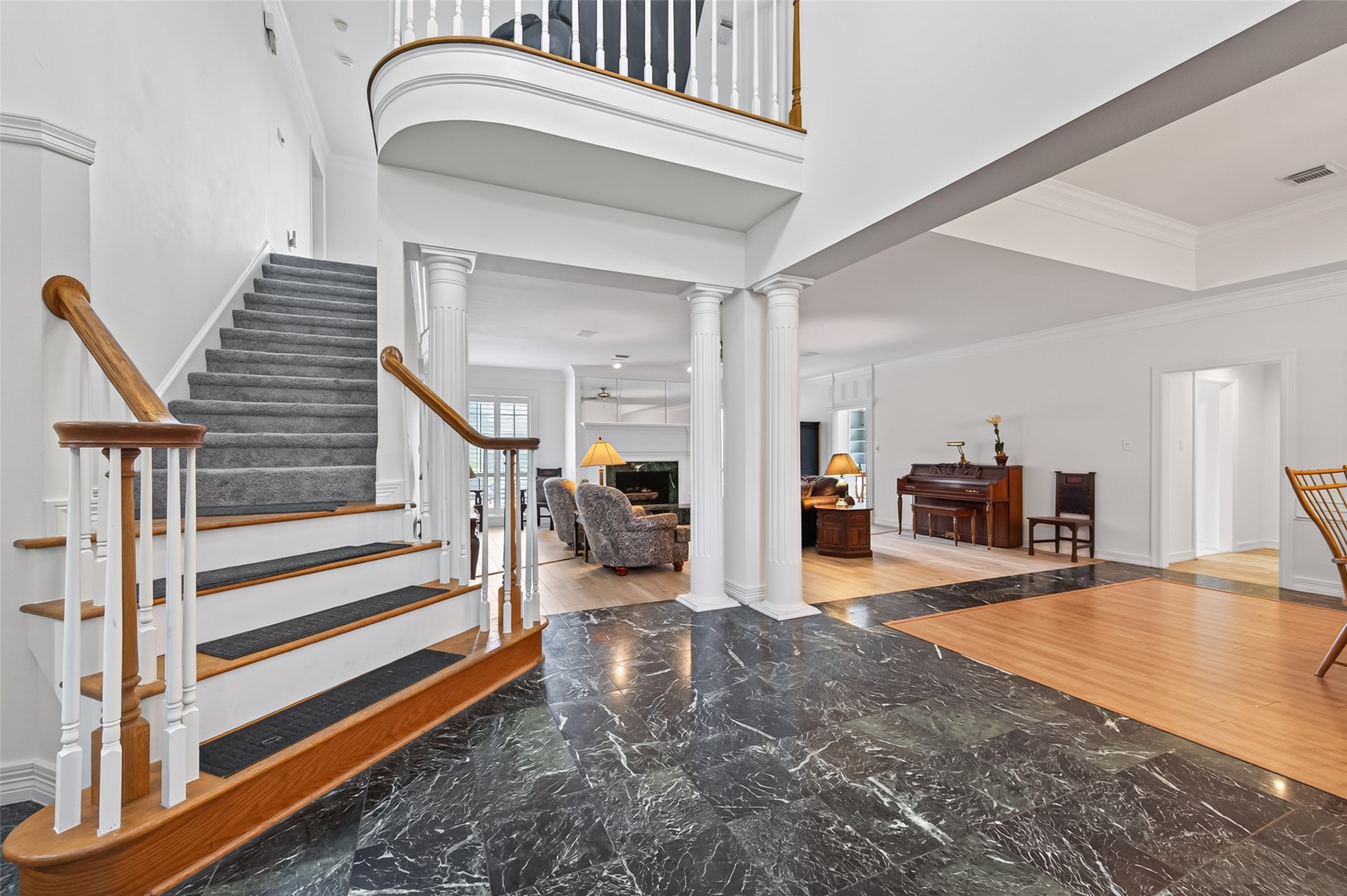 Elegant entryway featuring a grand staircase with custom flooring and classic columns, seamlessly leading into a spacious living area.