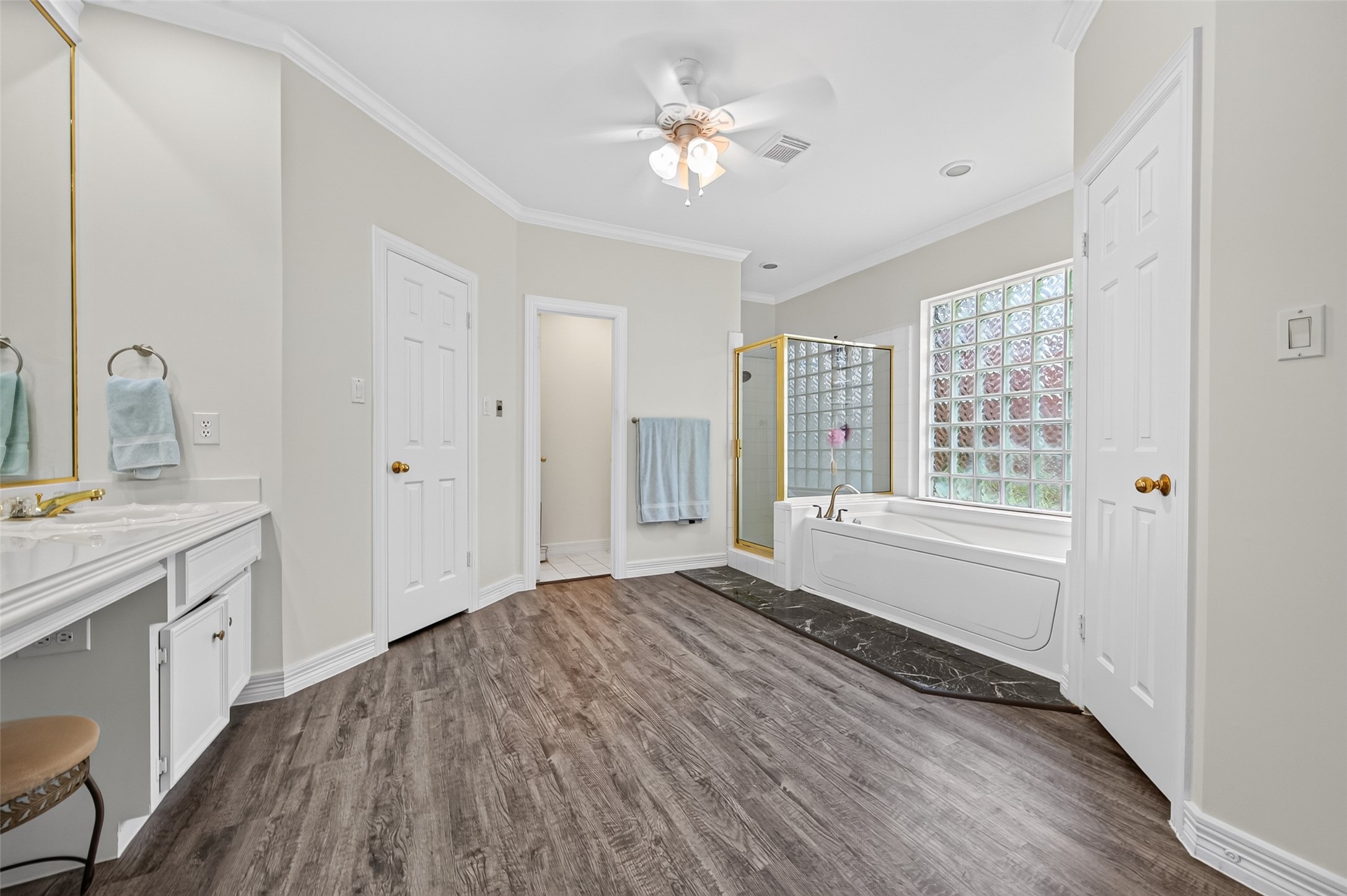 Spacious bathroom featuring elegant flooring, a luxurious soaking tub with a glass block window, separate shower, and a dual vanity with ample storage.