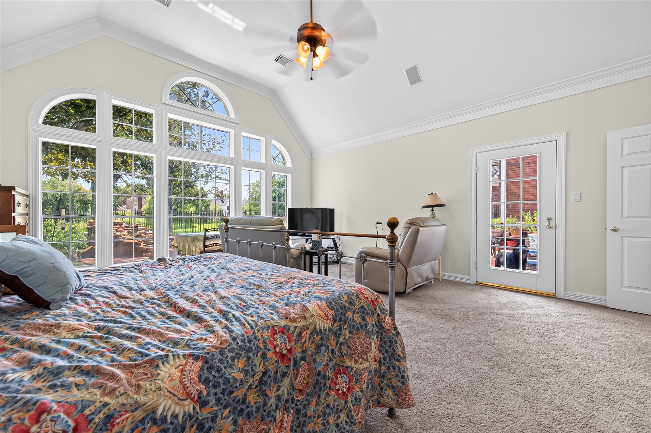 Expansive primary bedroom with vaulted ceilings and abundant natural light from beautiful large arched windows, offering a serene view of the backyard oasis and its own private access.