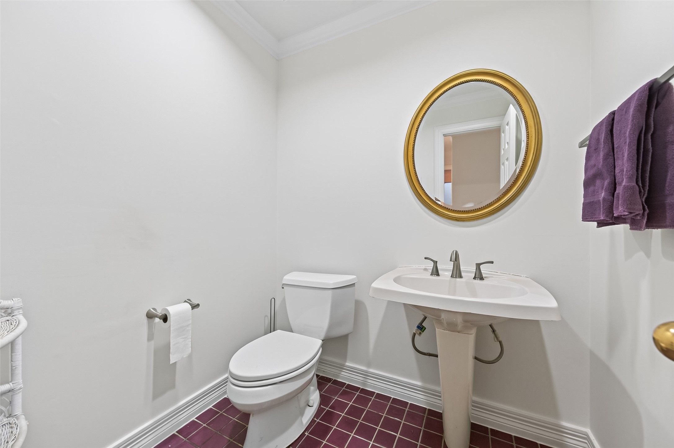 Charming powder room with elegant maroon tile flooring, a pedestal sink, and a classic oval mirror with a gold frame.