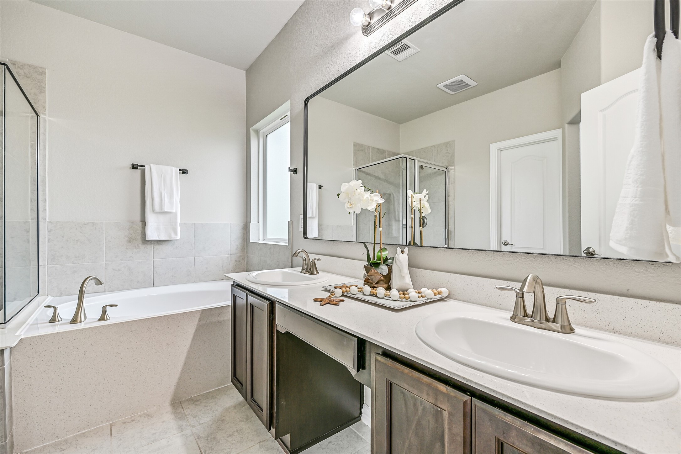 The spacious primary bath features separate his-and-her vanities, generous counter space, and a large framed mirror that enhances the room's bright, open feel while making busy mornings easy to navigate.