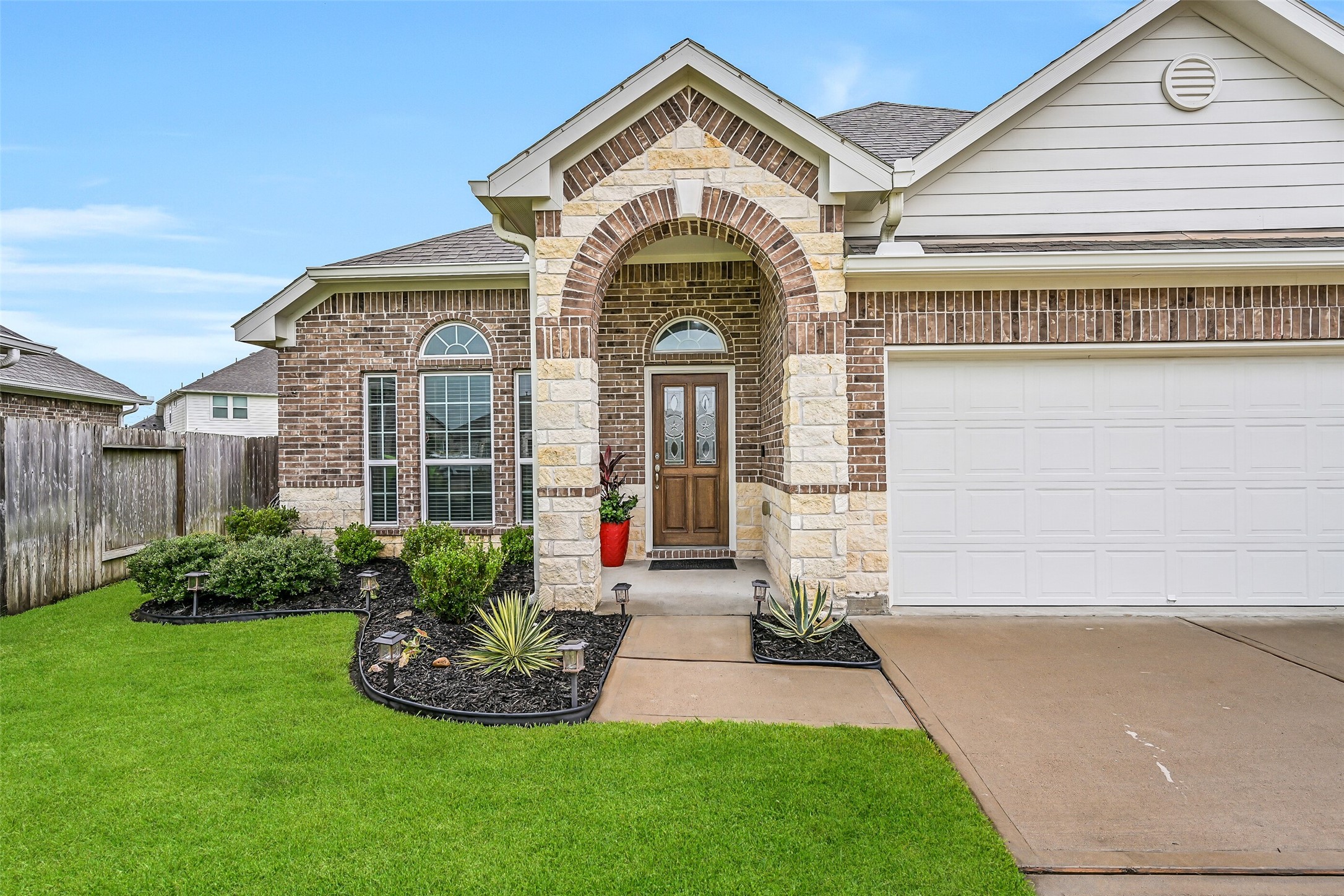 Stone columns, an impressive covered front porch, and a decorative glass front door create a warm first impression. Fresh mulch, manicured landscaping, and architectural details enhance the welcoming feel before you even step inside.
