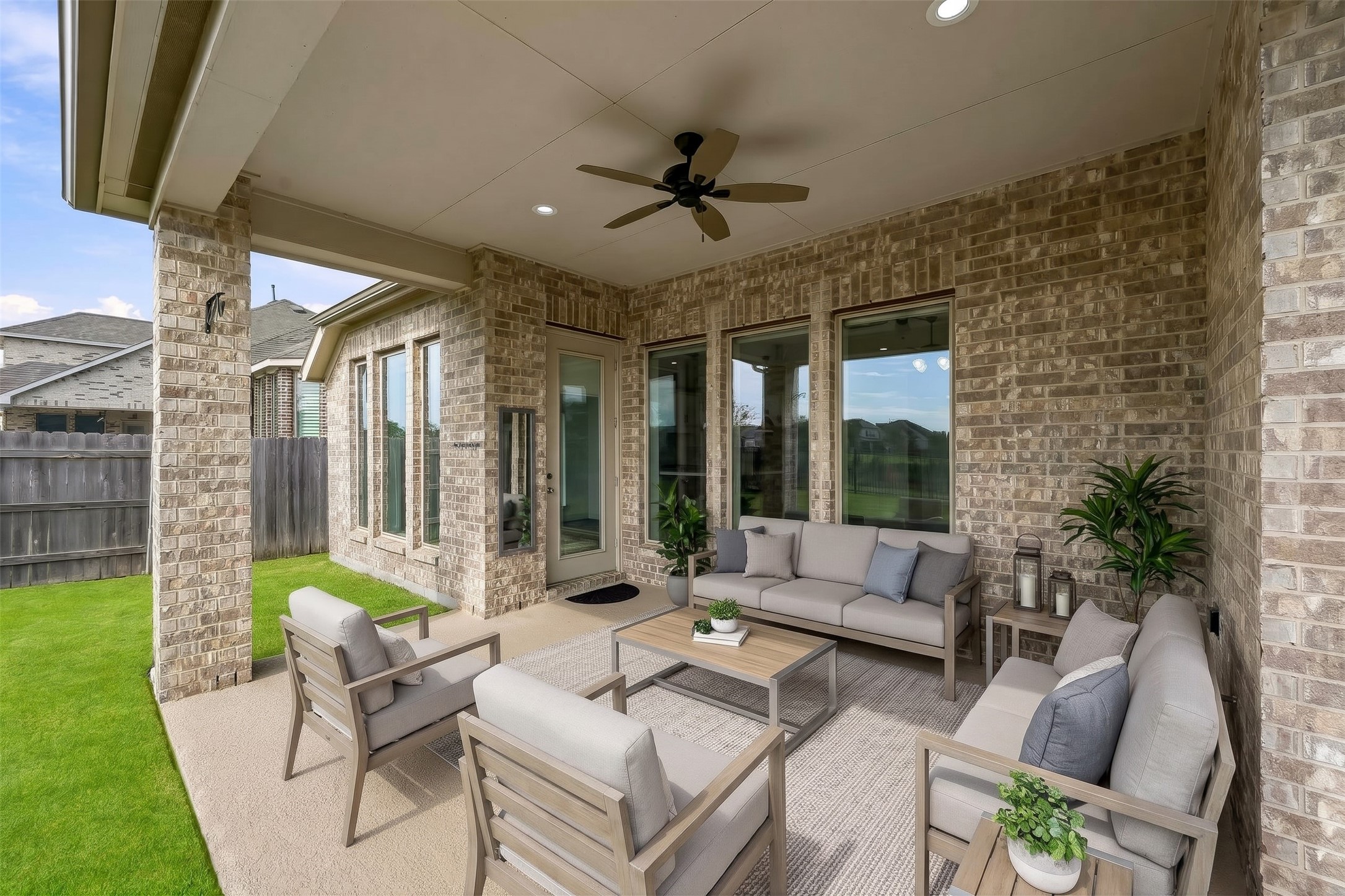 Virtually Staged: A sheltered outdoor retreat, this expansive covered patio offers seamless flow into the backyard. The solid brick structure, durable slab flooring, integrated overhead lighting, and cooling fan combine to create a versatile footprint suited for gathering in any season.