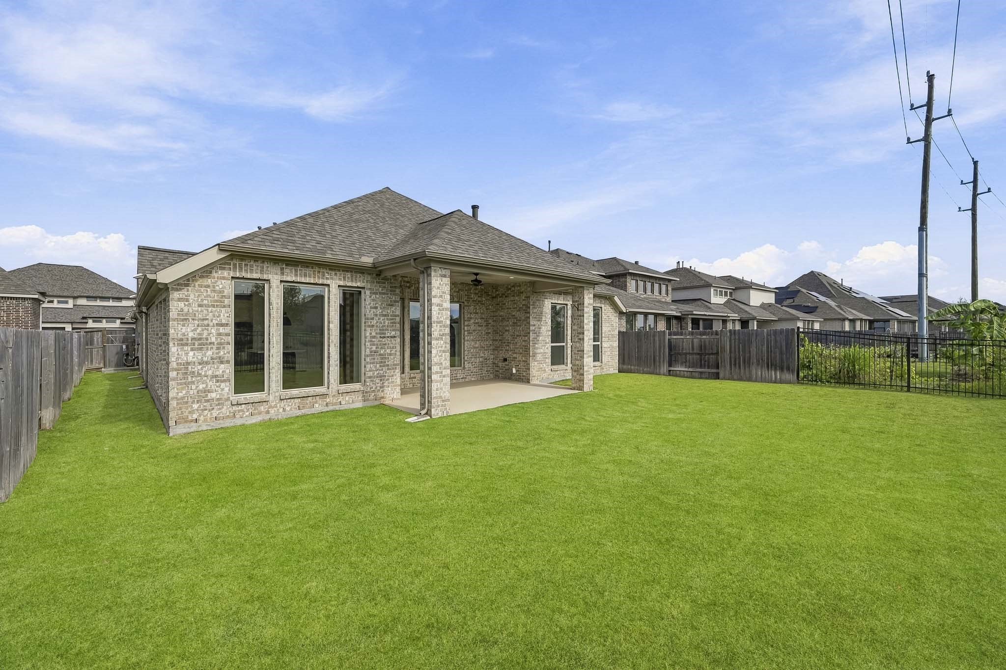 This property boasts a substantial backyard featuring an expansive, level lawn bordered by perimeter fencing. The exterior design is anchored by an all-brick facade and a generous covered back patio supported by substantial brick columns, offering seamless indoor-outdoor living with views of the vast green space.