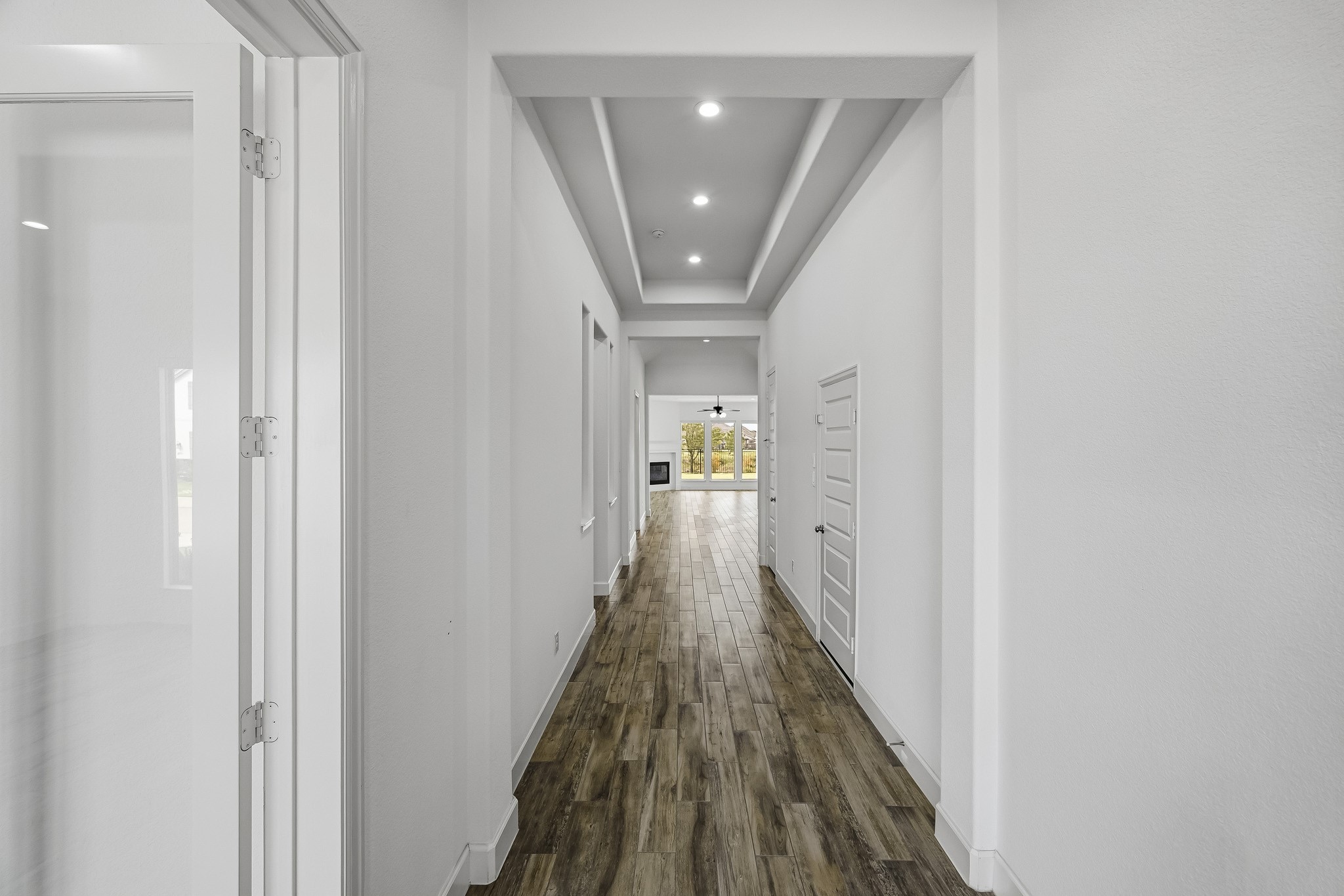 Generously proportioned with dramatic ceiling recesses, this central pathway accentuates the home's open and airy layout. Seamless wide-plank flooring spans the entire corridor, establishing an elegant visual bridge from the foyer to the sweeping living area beyond.