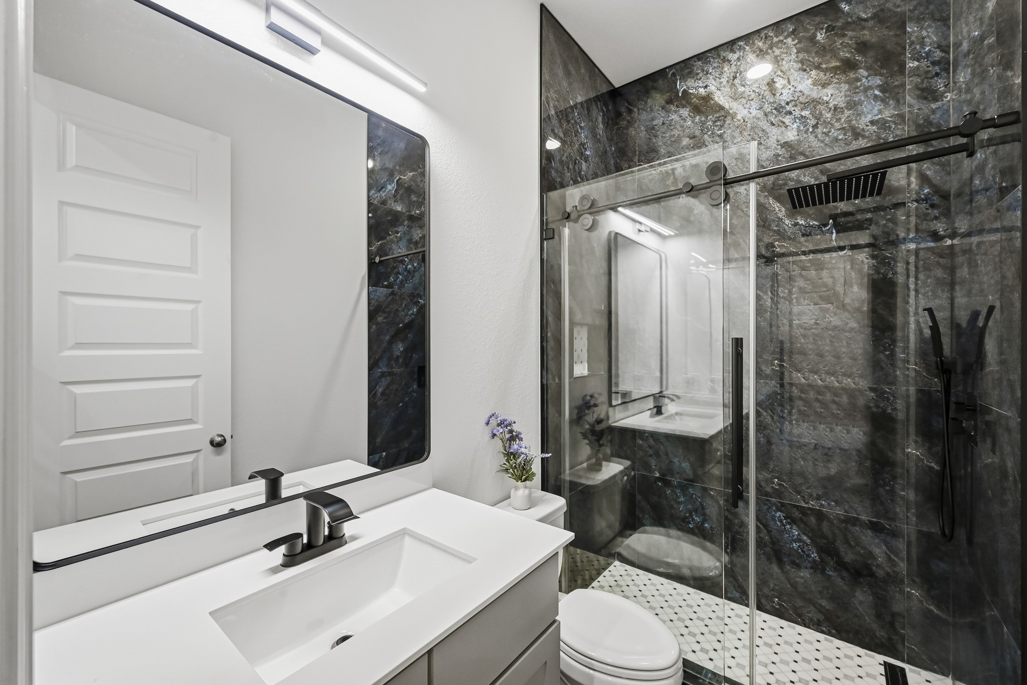 This modern bathroom showcases high-end finishes, highlighted by a spacious walk-in shower enclosed in sliding glass. Striking stone-look wall panels line the shower interior, beautifully paired with geometric tile flooring, an undermount sink basin, and an expansive wall mirror that enhances the room's open feel.