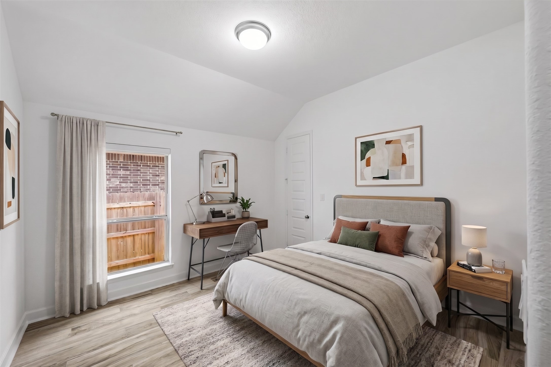 Virtually Staged: This secondary bedroom features vaulted ceilings and wood-style flooring, creating an open and balanced atmosphere. A tall exterior window provides abundant natural light, highlighting the room's generous proportions and clean layout.