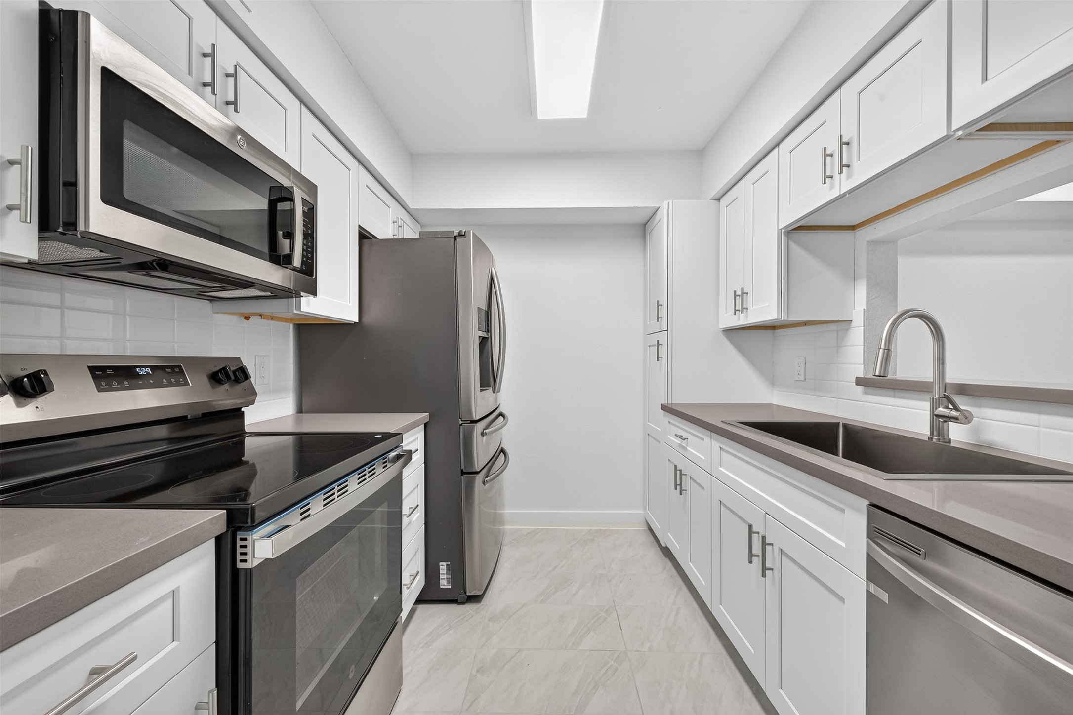 Beautifully redesigned kitchen showcasing Concrete Grey quartz countertops, white shaker cabinetry, brushed nickel hardware, and stainless steel appliances.