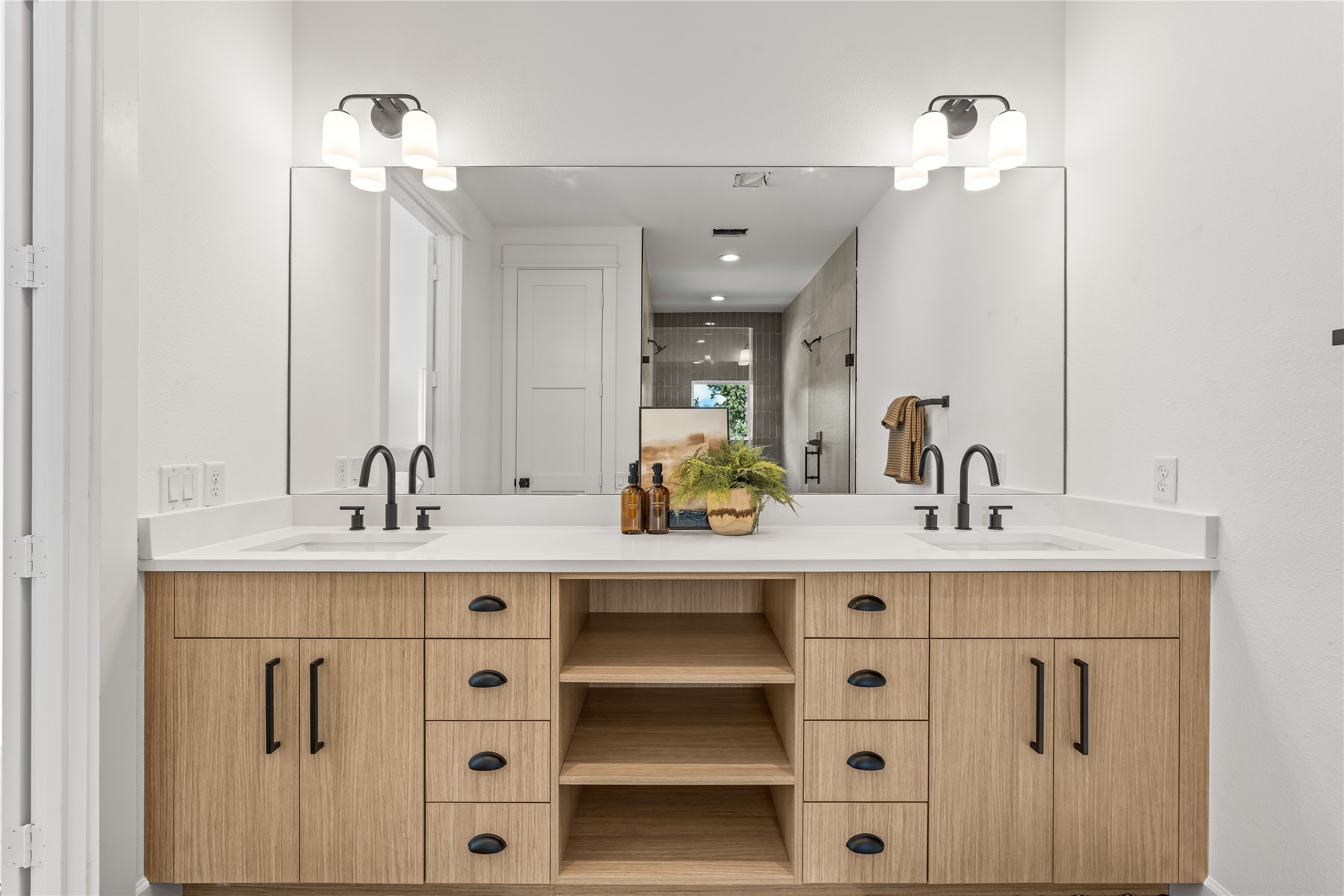 Straight-on view of the primary en-suite bathroom's expansive double vanity with light wood cabinetry, open shelving, and black hardware.