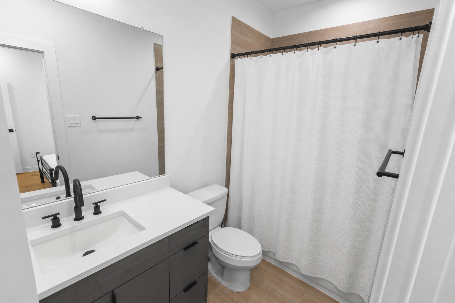 Bright ensuite first floor bath showcases crisp white quartz countertops, contemporary cabinetry, matte black hardware, and a full tub and shower combination. Neutral finishes provide a clean, modern look that complements the homes cohesive design throughout.