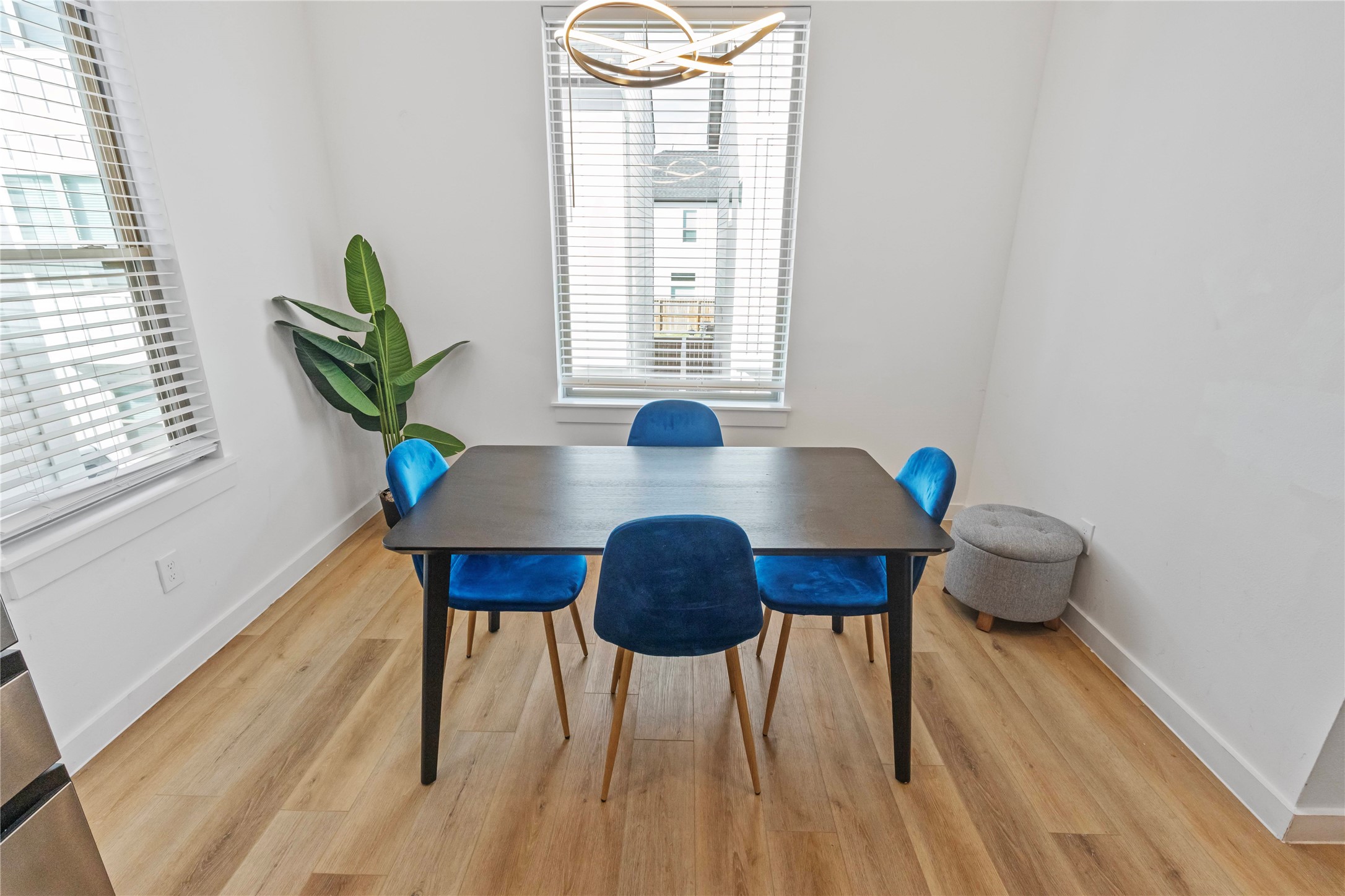 Sunlit dining space is framed by windows on two sides, creating a bright setting for everyday meals or entertaining. Contemporary lighting and warm wood look flooring complement the open connection to the kitchen and living areas.