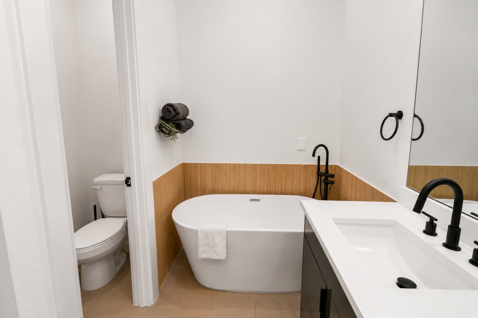 Relax and recharge in a spa inspired primary bath featuring a freestanding soaking tub framed by warm fluted wood accent paneling, quartz countertops, and sleek matte black fixtures. A separate water closet and clean, contemporary finishes create a private retreat with timeless designer appeal.