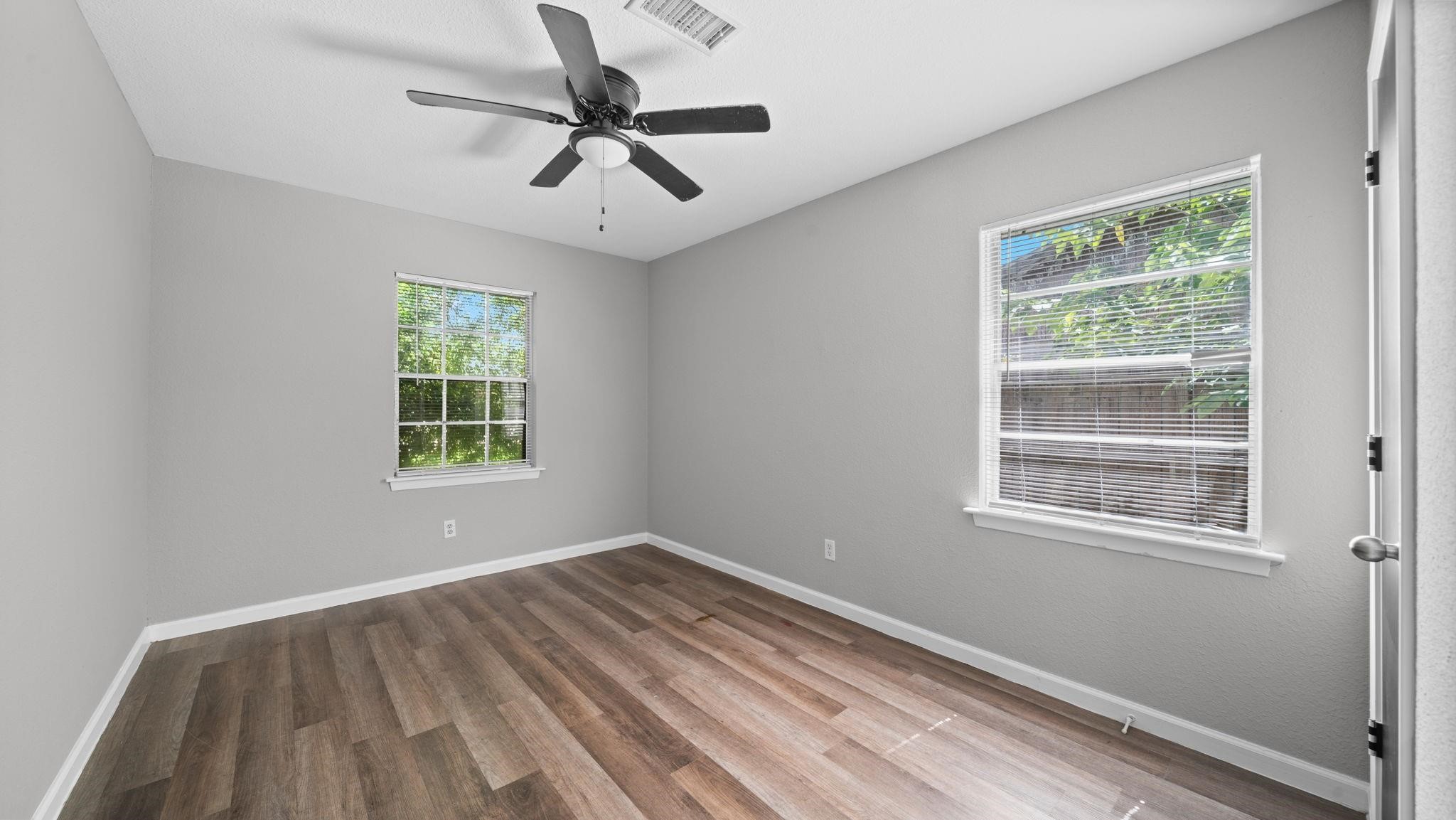 This well-appointed secondary bedroom features luxury vinyl flooring, two windows with blinds that welcome natural light, and a ceiling fan with integrated lighting. A spacious walk-in closet provides ample storage, completing this comfortable and inviting retreat.