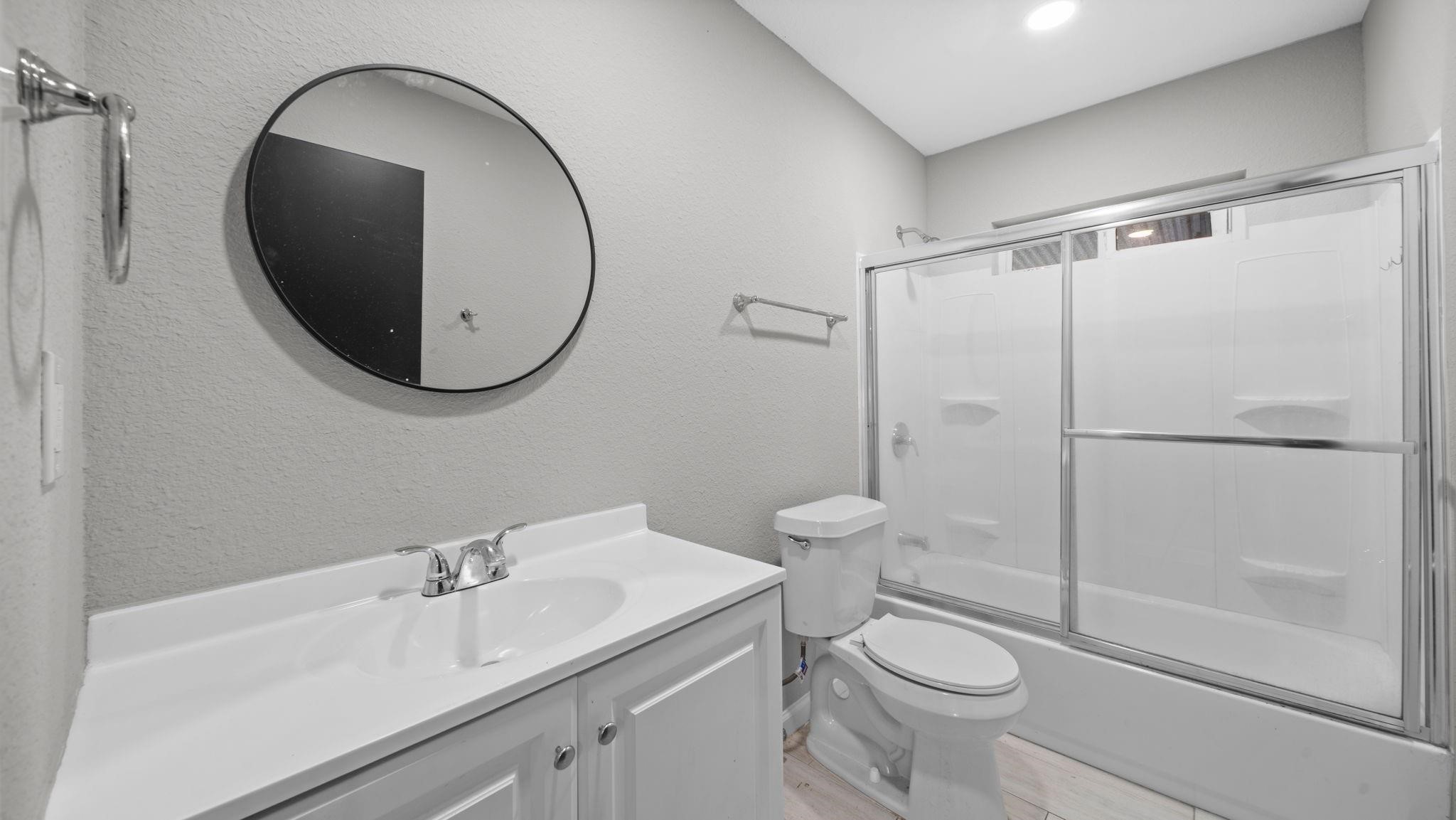 The secondary bath features elegant 12 x 24-inch tile flooring, a cultured marble vanity, and recessed lighting for a clean, contemporary aesthetic. A tub/shower combination with a sliding glass door is complemented by a window above the shower, inviting natural light into the space.