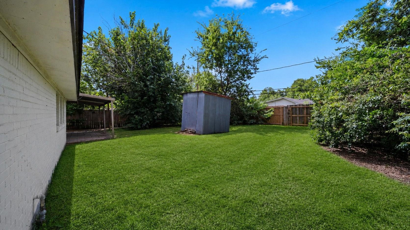 A corrugated steel storage shed provides convenient space for tools and outdoor essentials, while an additional patio area creates an inviting setting for outdoor dining and relaxation. The expansive backyard offers endless possibilities for lush landscaping, recreation, or creating a personalized outdoor retreat.