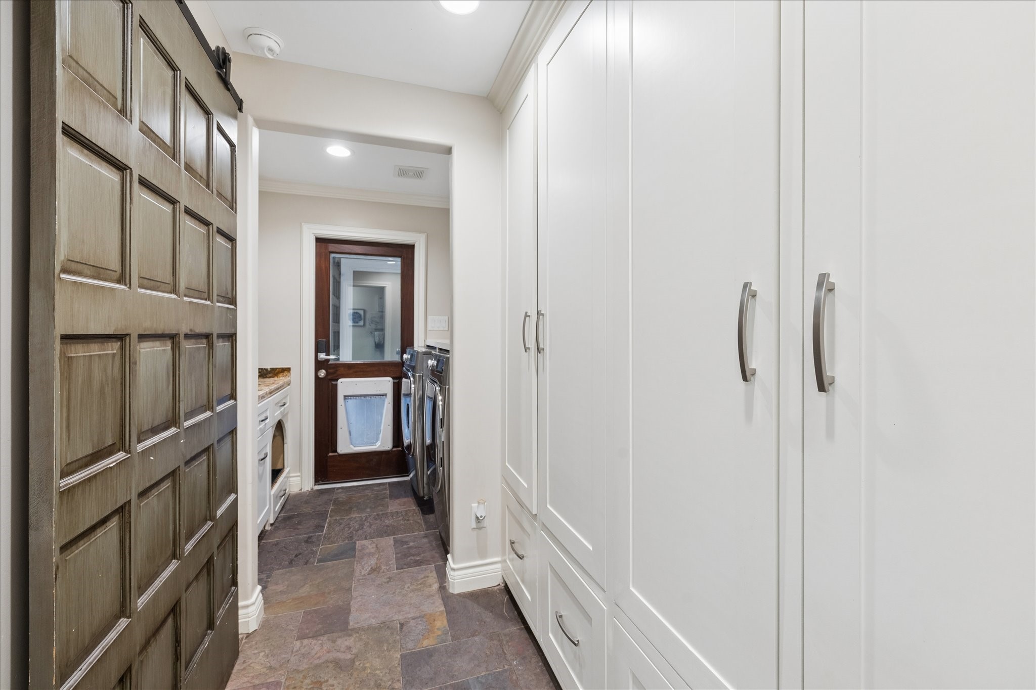 Mudroom with lockers and laundry room with folding counter. Door in background leading to garage.