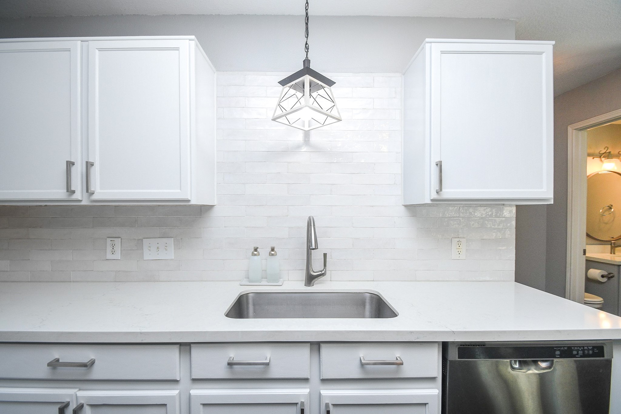 Sleek kitchen with modern white cabinetry, a stylish backsplash, and stainless steel appliances, highlighted by elegant pendant lighting above the sink.