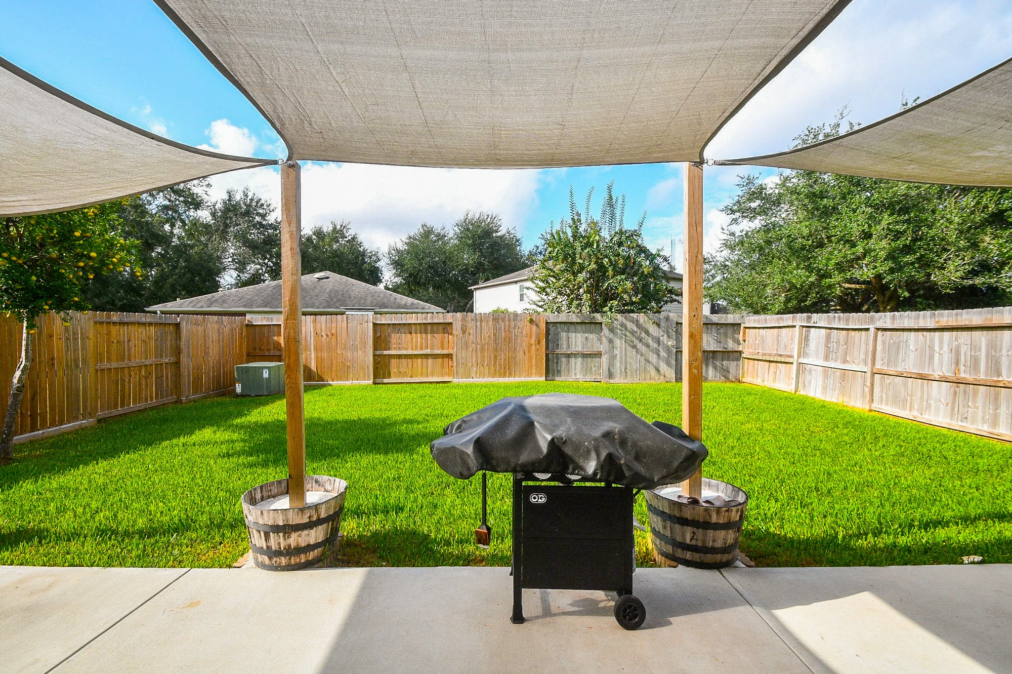Spacious backyard retreat features lush green lawn, shaded patio with sail canopies, and a barbecue grill, perfect for outdoor entertaining.