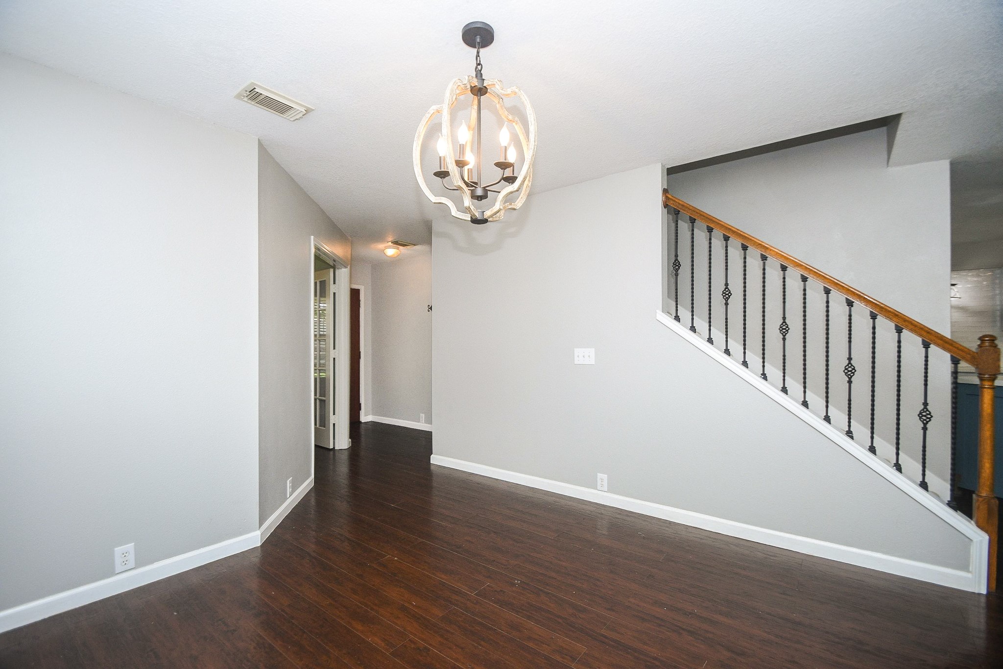 Bright and inviting hallway with elegant dark wood flooring, modern light fixture, and stylish staircase with wrought iron details.