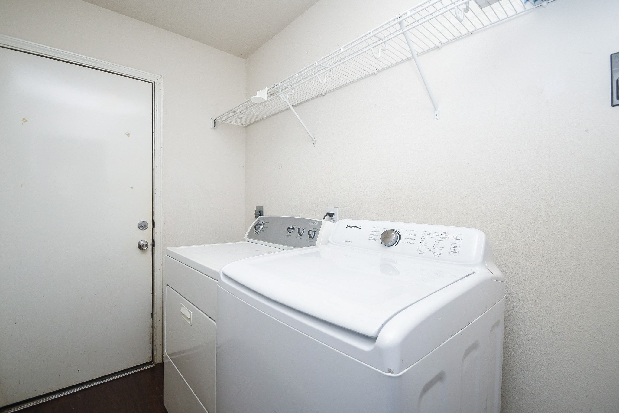 Convenient laundry room equipped with a washer and dryer, featuring a shelf for storage and a door for easy access.