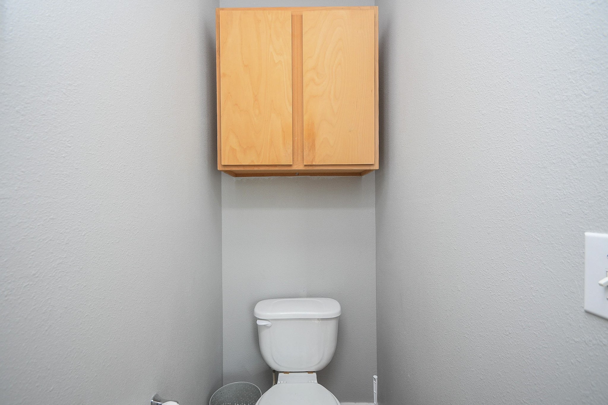Compact bathroom featuring a modern toilet and overhead storage cabinet, set against neutral gray walls.