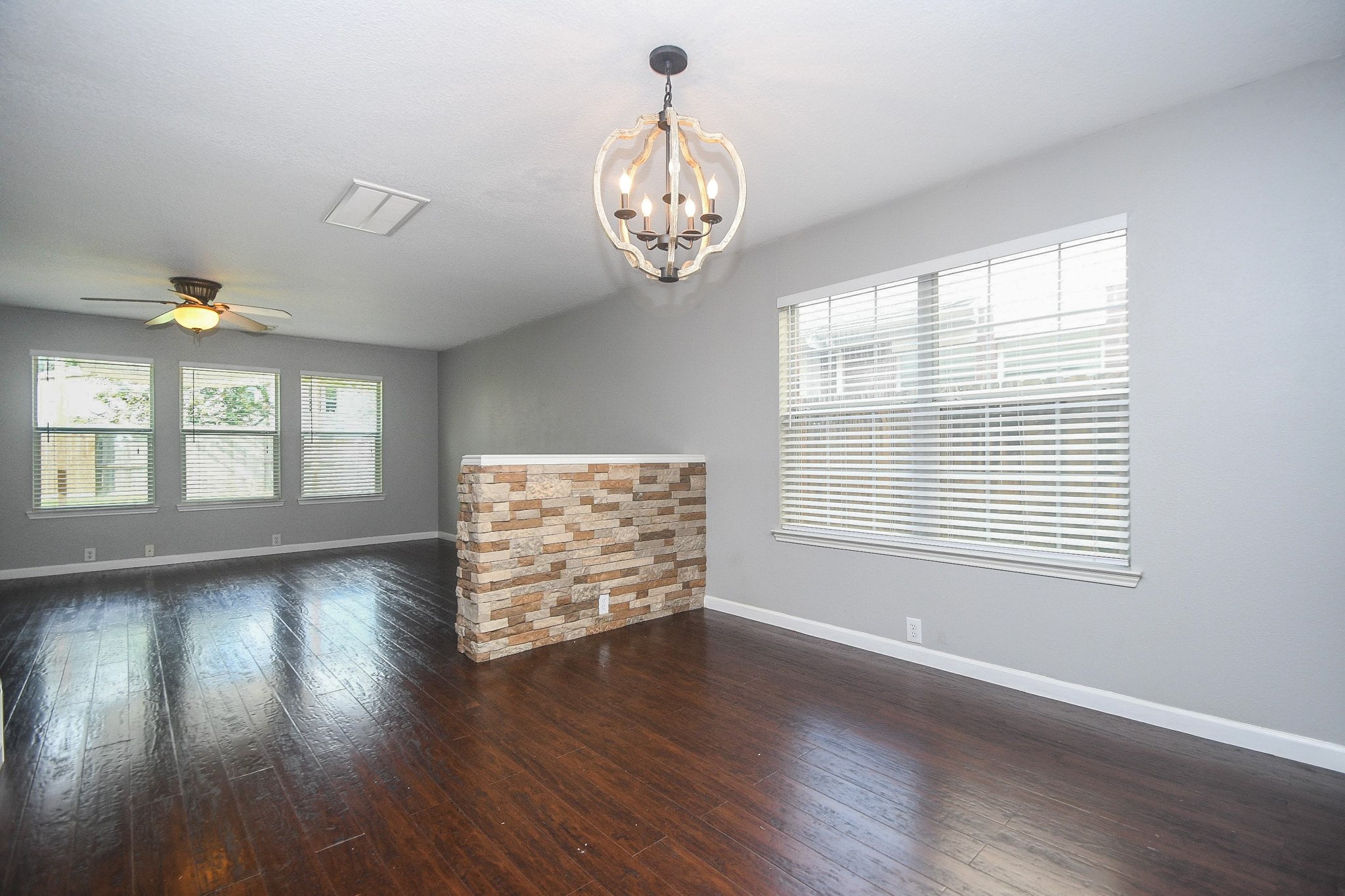 Spacious living area with rich laminate hardwood floors, large windows for natural light, and a stylish stone accent wall.