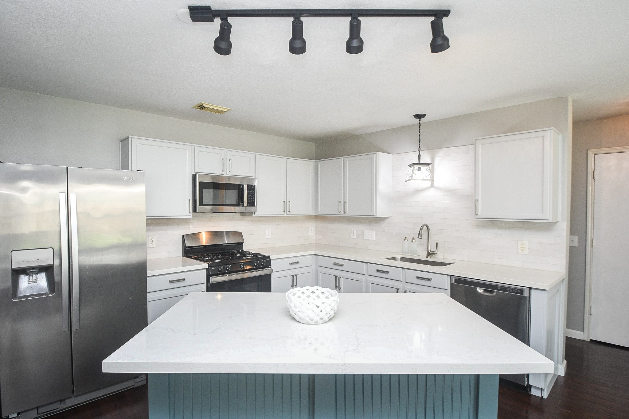 Modern kitchen featuring sleek stainless steel appliances, white cabinetry, and a spacious island with elegant lighting.