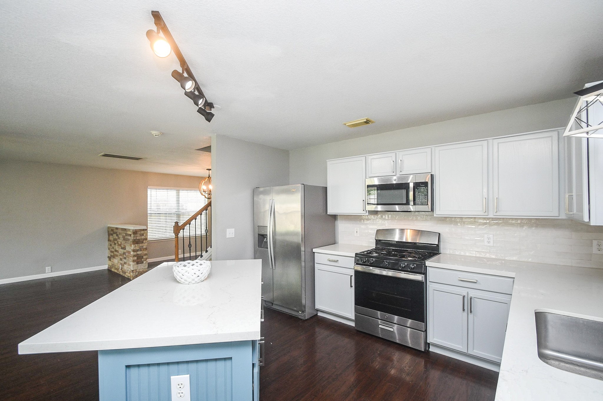 Bright, modern kitchen featuring stainless steel appliances, white cabinetry, and a sleek island with a contrasting blue base.