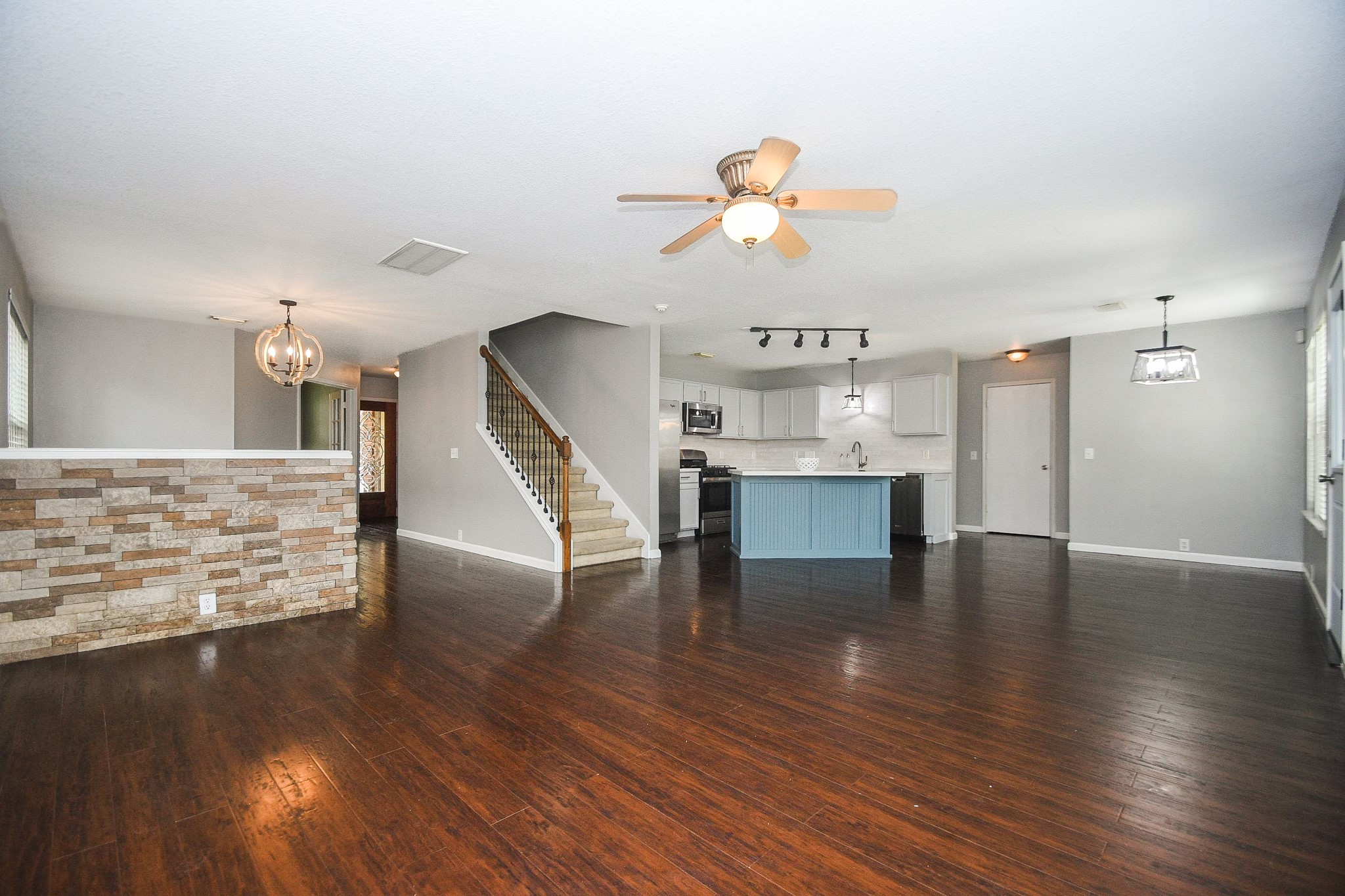 Spacious open-concept living area with rich hardwood floors, a modern kitchen featuring a stylish blue island, and elegant lighting fixtures. The space includes a cozy dining area and a staircase with wrought iron railing, perfect for both entertaining and everyday living.