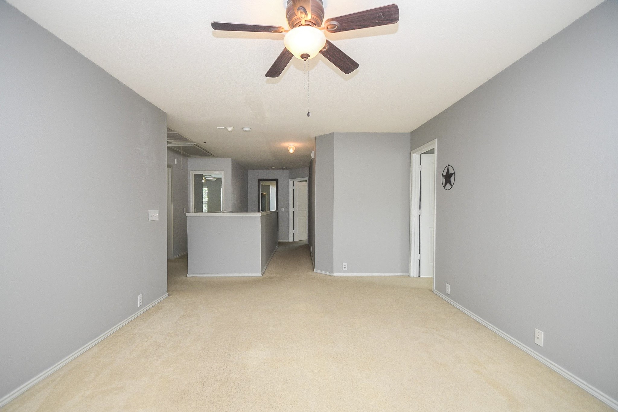 Spacious living area with neutral tones, featuring a ceiling fan and ample natural light, leading to a cozy hallway.