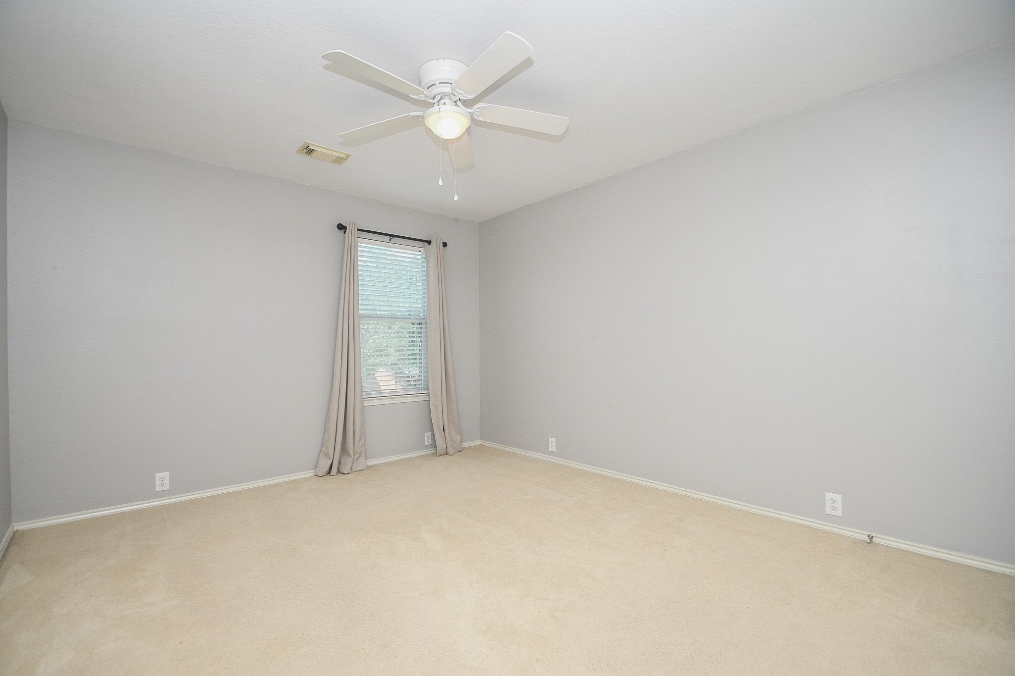 Spacious room with neutral walls, plush carpeting, and a ceiling fan, featuring a large window for ample natural light.