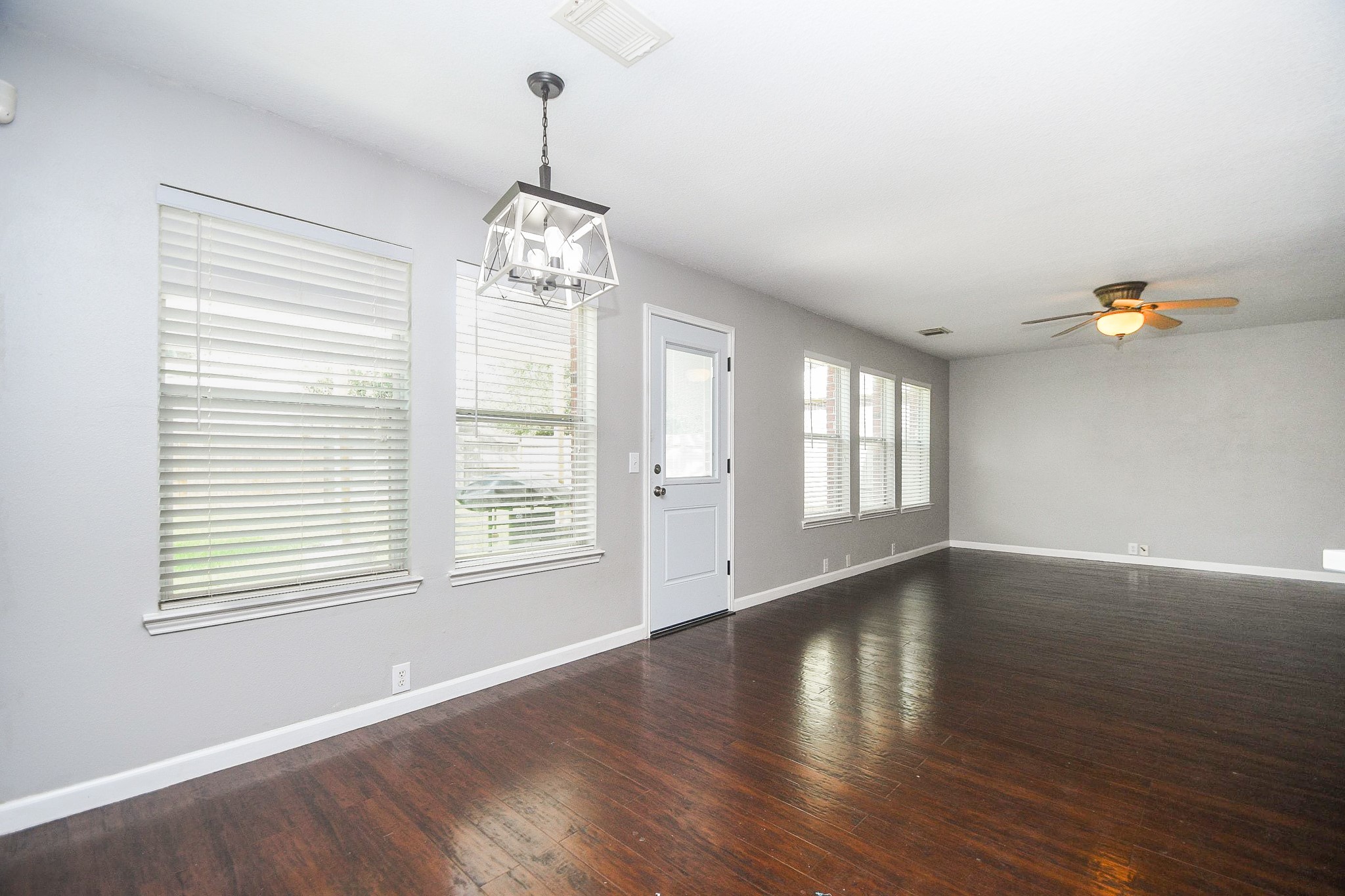 Spacious living area with rich hardwood floors, abundant natural light from multiple windows, and modern fixtures including a ceiling fan and stylish light fixture.
