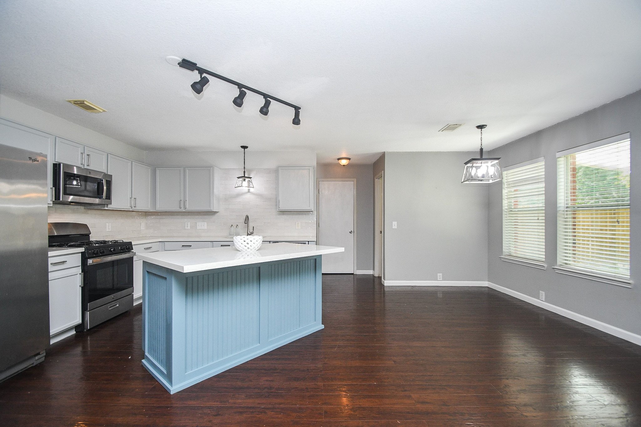 Spacious kitchen with a stylish blue island, stainless steel appliances, and sleek cabinetry, seamlessly connecting to a bright dining area with ample natural light.
