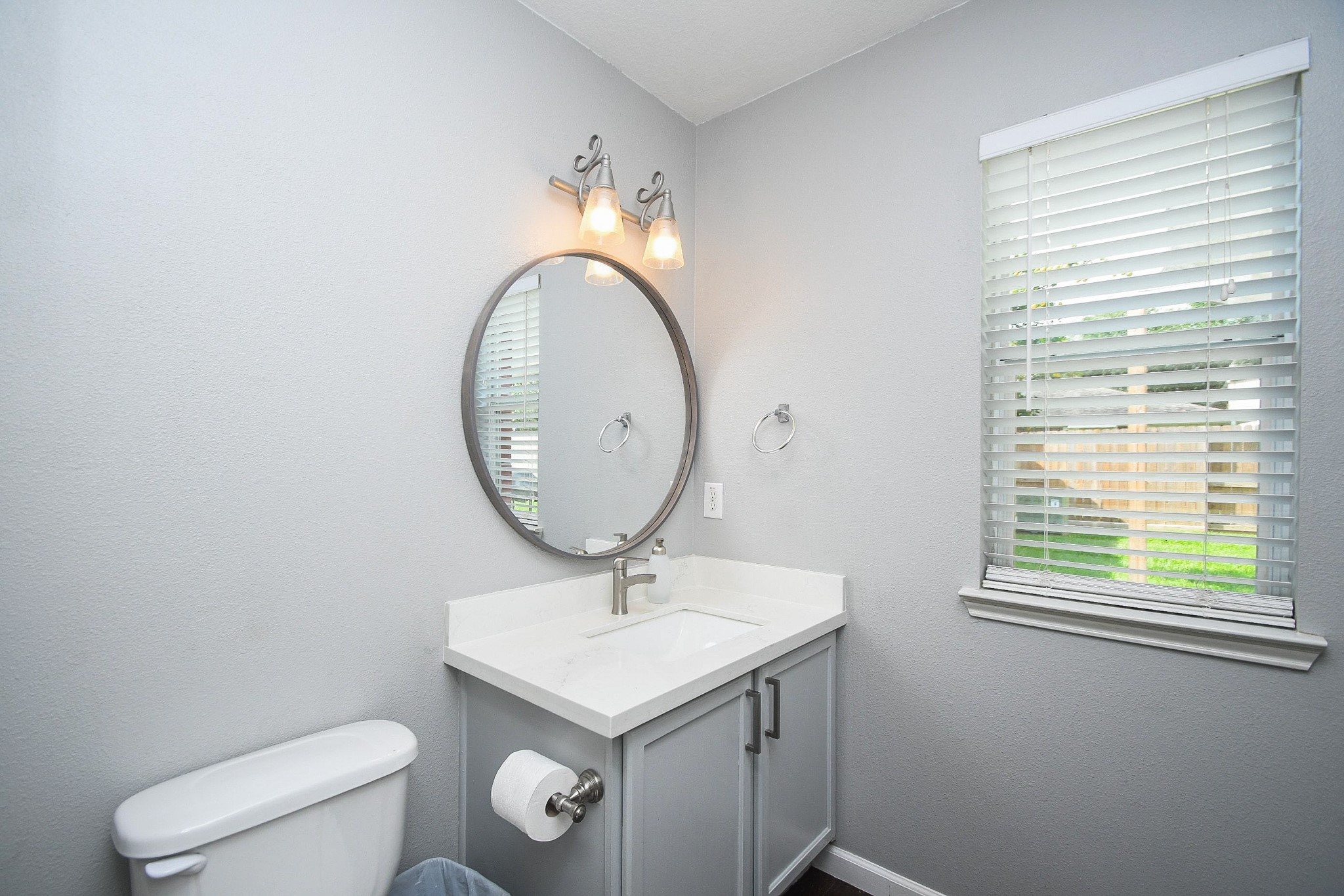 Bright and modern bathroom featuring a sleek vanity with a round mirror, complemented by soft lighting and a window for natural light.