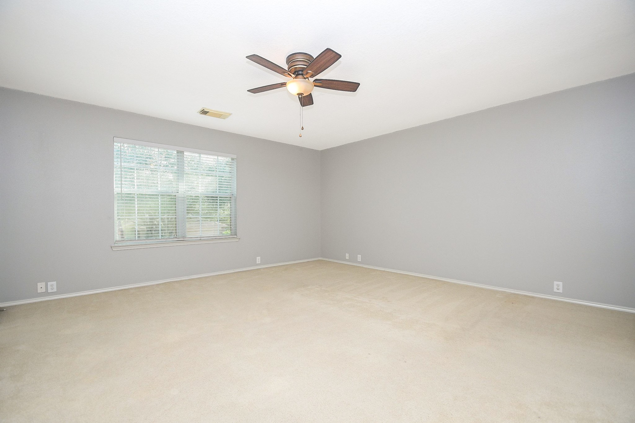 Spacious bedroom with soft carpet, neutral gray walls, and a ceiling fan, offering ample natural light through a large window.